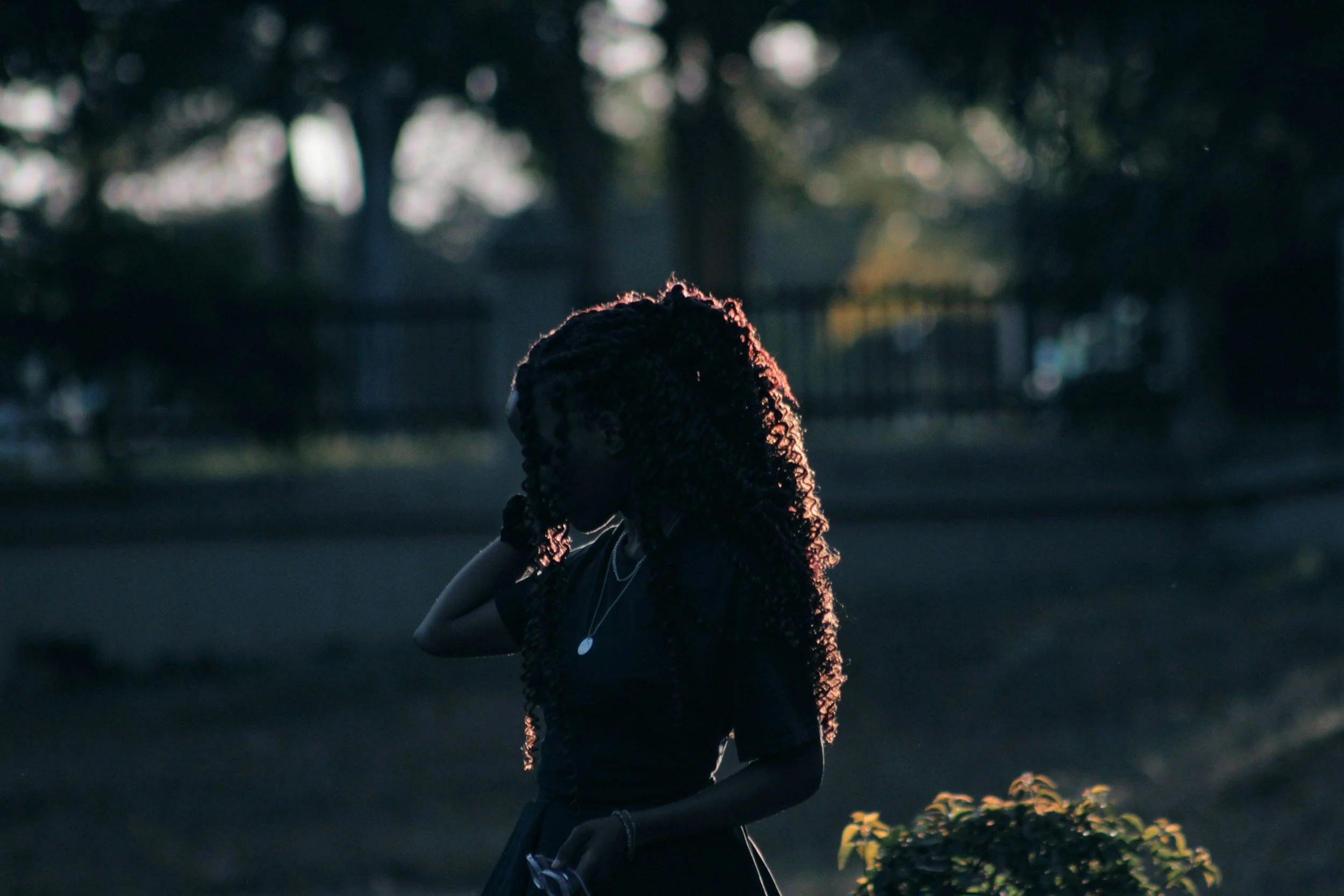 A dark, high-contrast silhouette portrait of a woman with curly hair standing outside in low light, serving as a cinematic author headshot inspiration example
