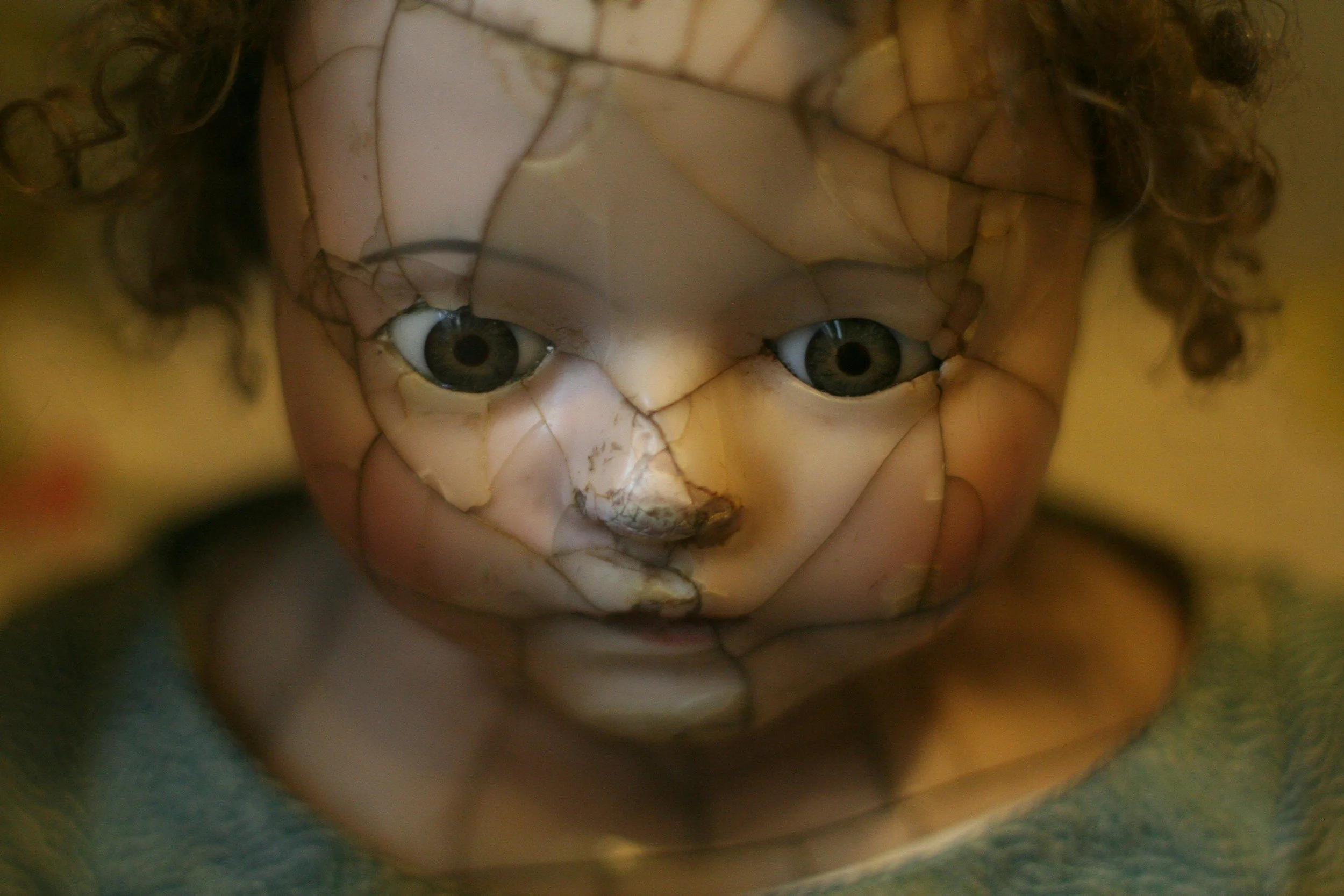 A close-up of a cracked porcelain doll's face with staring glass eyes, demonstrating a haunted aesthetic photo for thriller author branding
