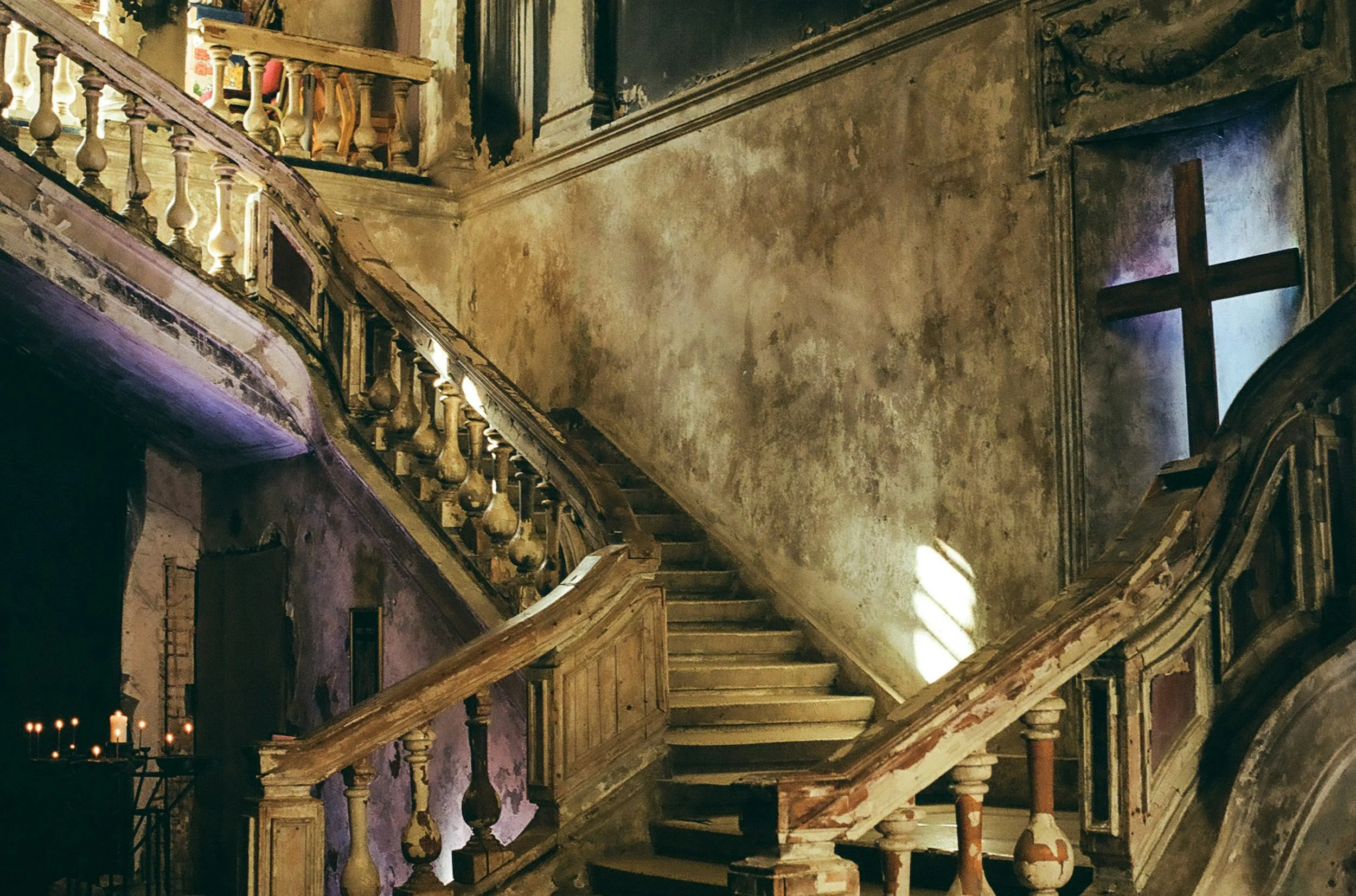 A decaying grand wooden staircase inside an old mansion with shafts of dramatic light, illustrating an editorial photography style for gothic writers