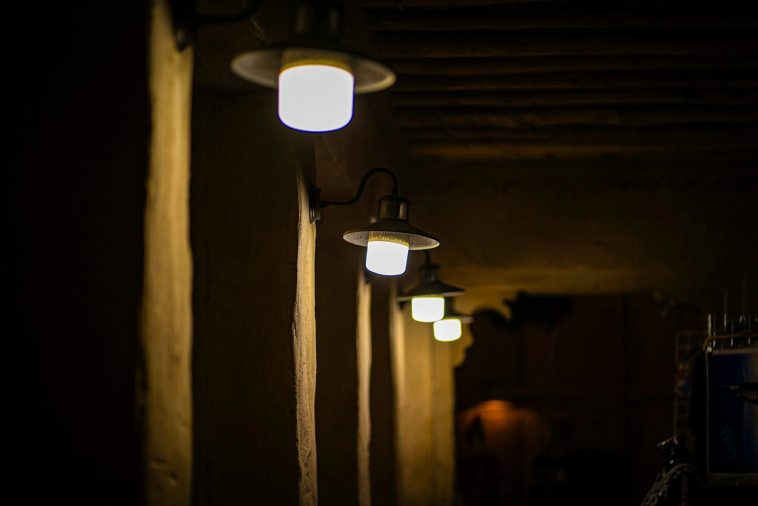 row of glowing industrial ceiling lamps illuminating a dim, moody hallway with yellow light, capturing a cinematic gothic horror aesthetic