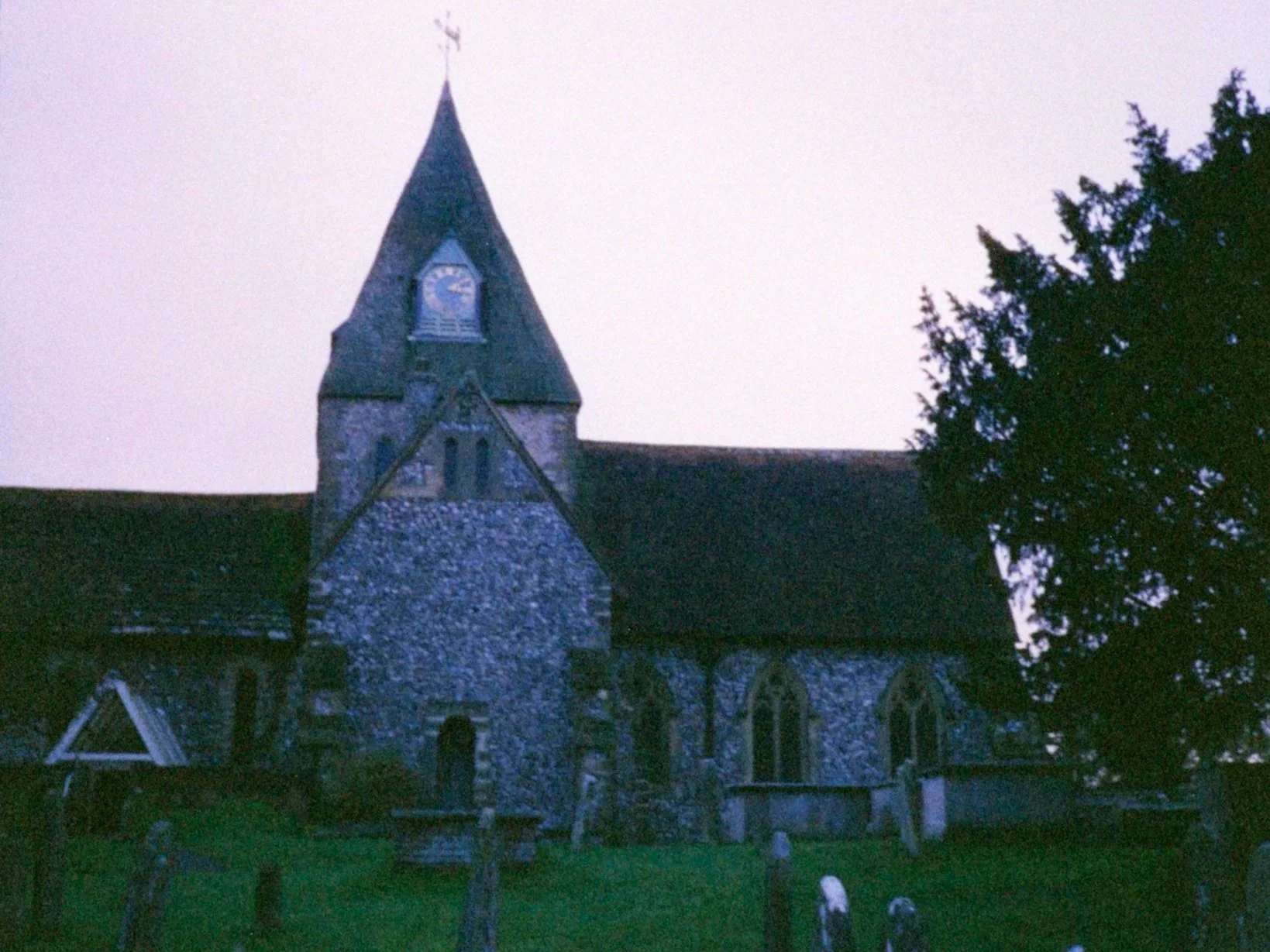 A historic stone church and graveyard captured under a pale twilight sky, illustrating moody gothic mystery author website imagery