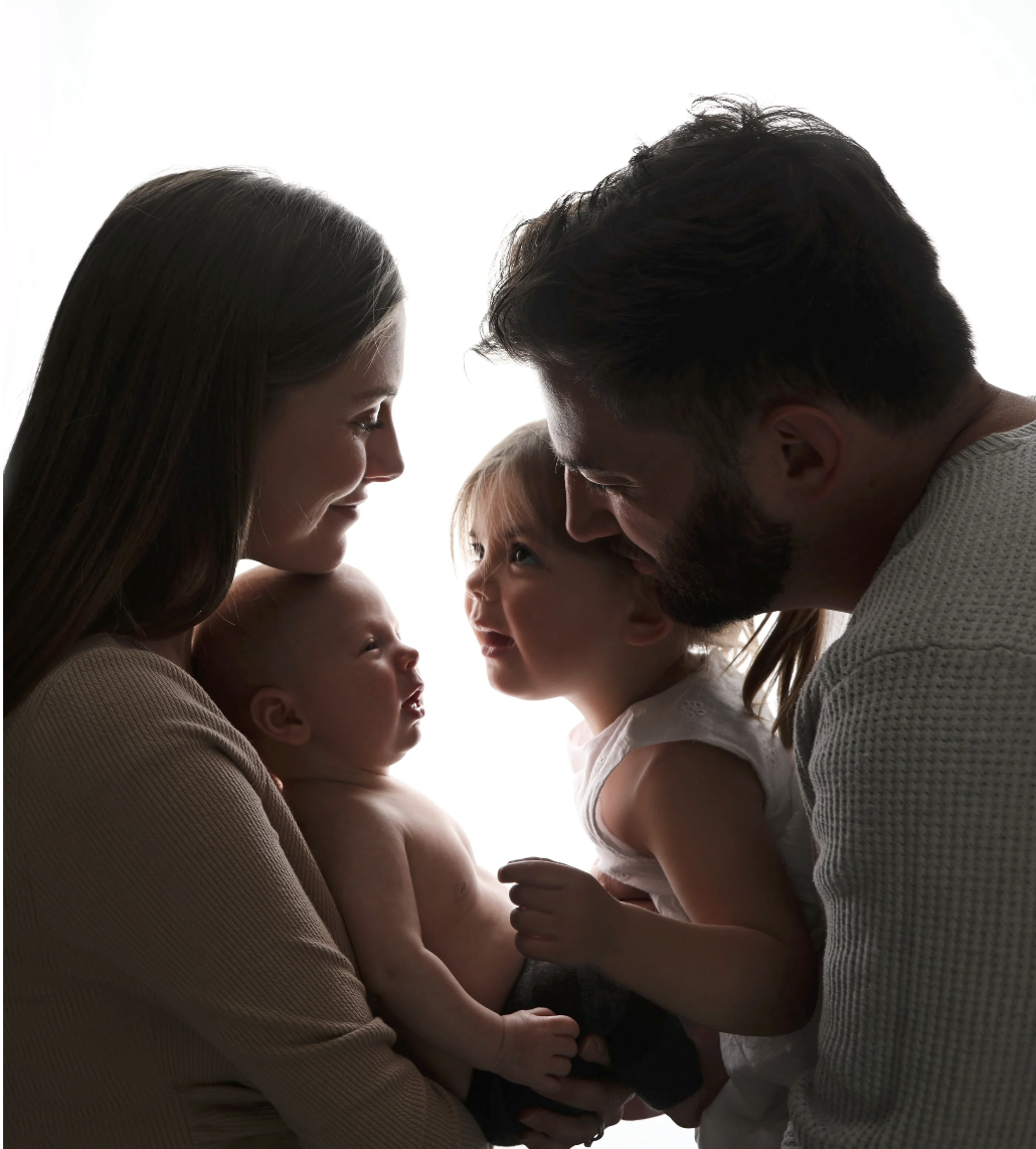 A family of four with two young children, a mother, and a father, silhouetted against a white background, all facing each other with smiles.