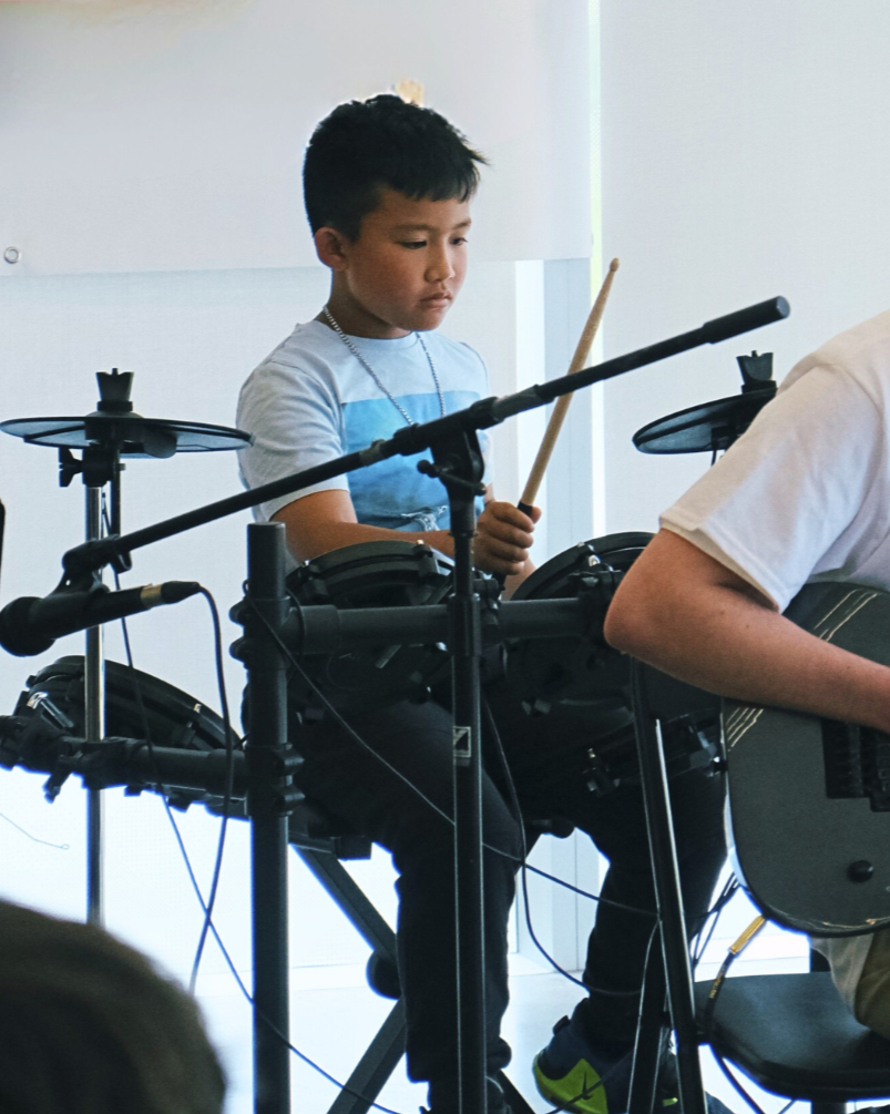 Close-up of young boy playing an electric drum kit within a group performance