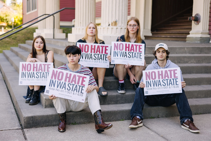 A group of teenagers sit on steps holding up campaign signs for No Hate in WA State
