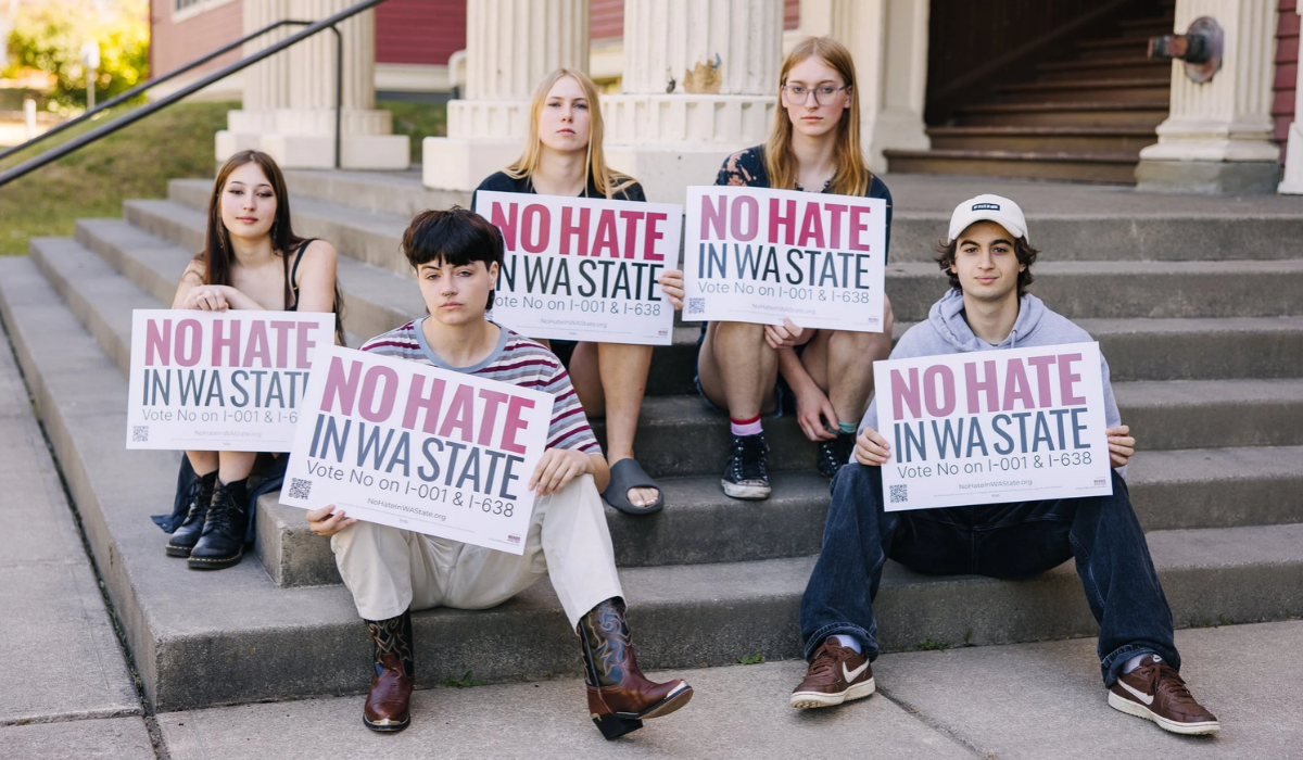 A group of young people sit on steps holding "No Hate in WA State" signs