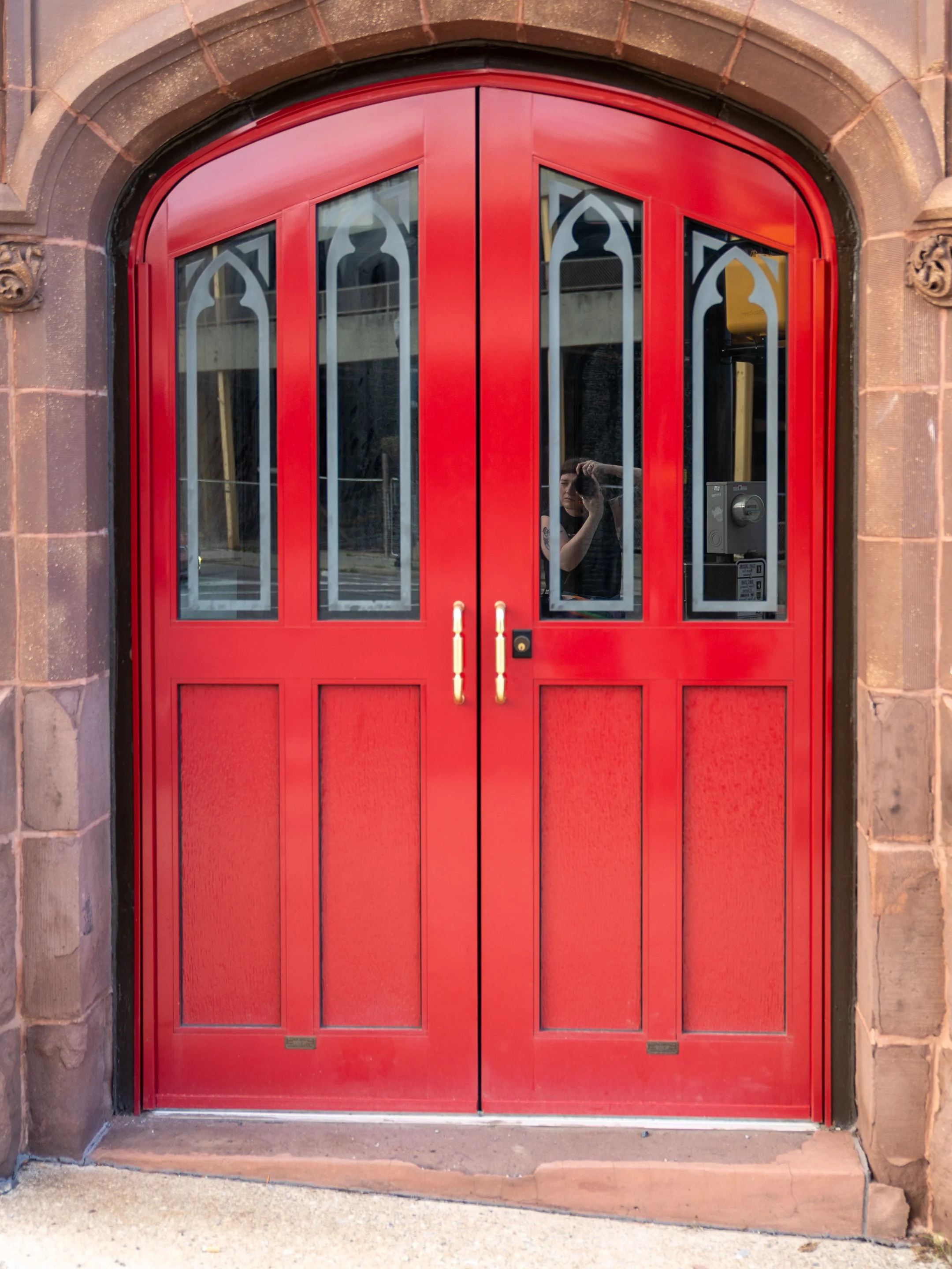 Red double door with arched windows, surrounded by brown stone and brick archway.