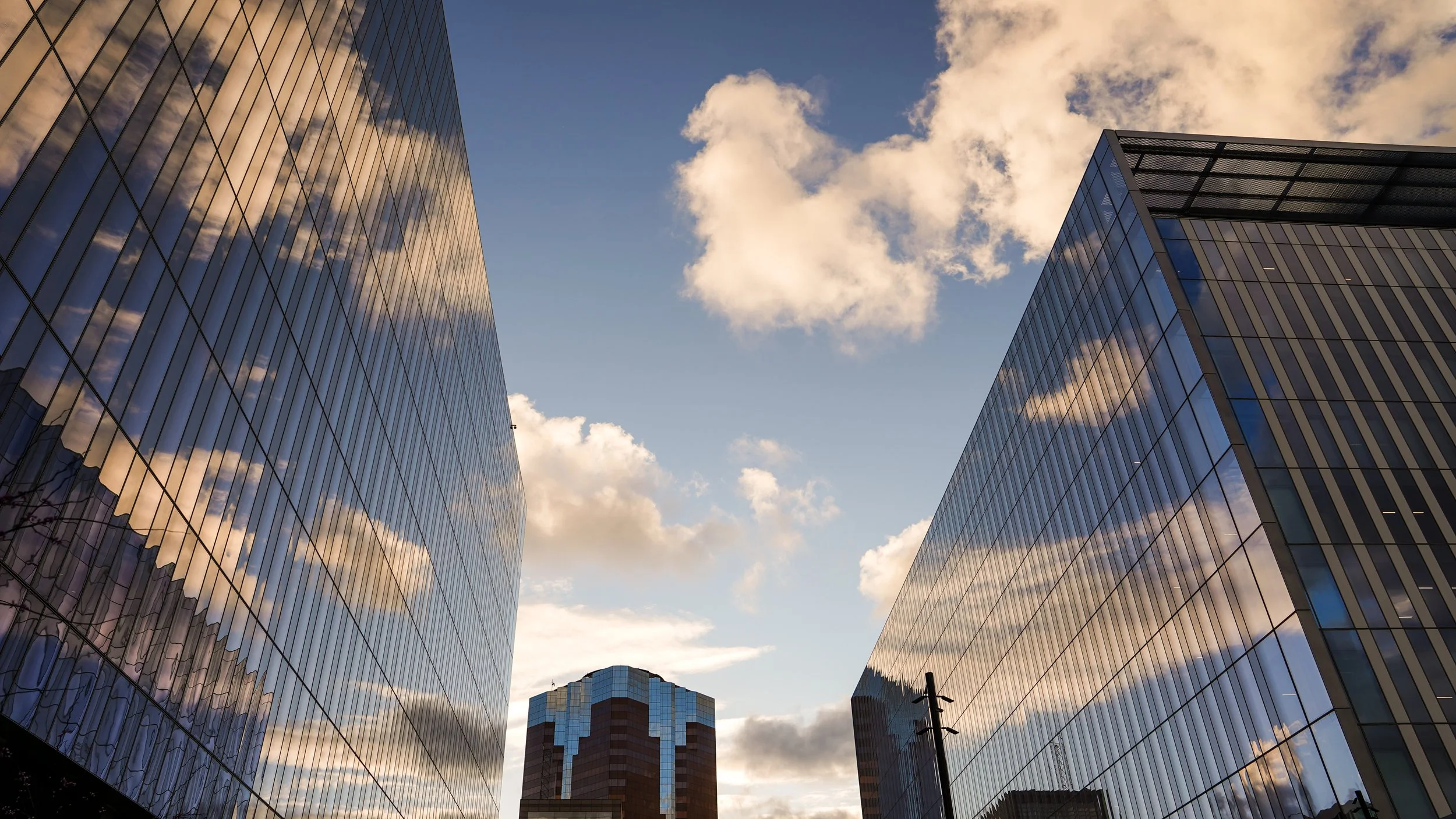 View of modern glass skyscrapers reflecting the sky with clouds, in an urban cityscape.