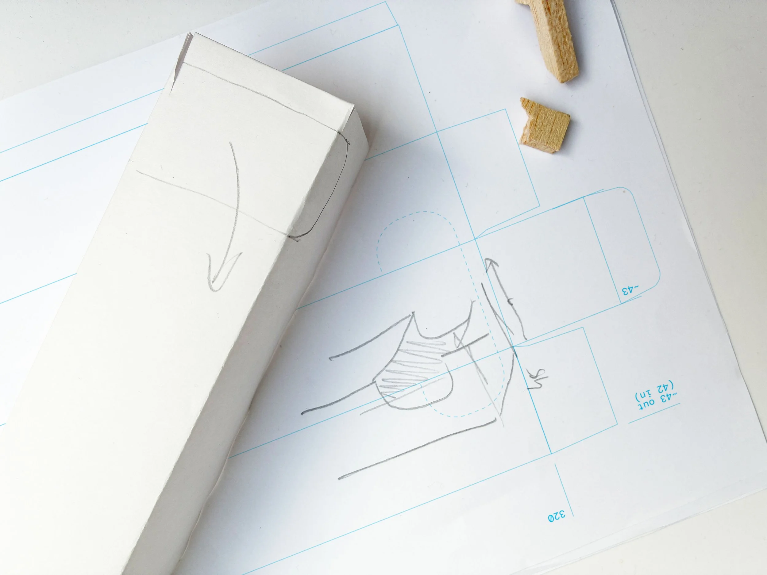 Innovative design drawing on paper with measurement annotations, a small partially visible wooden block, and a white block with black lines, all on a white surface.