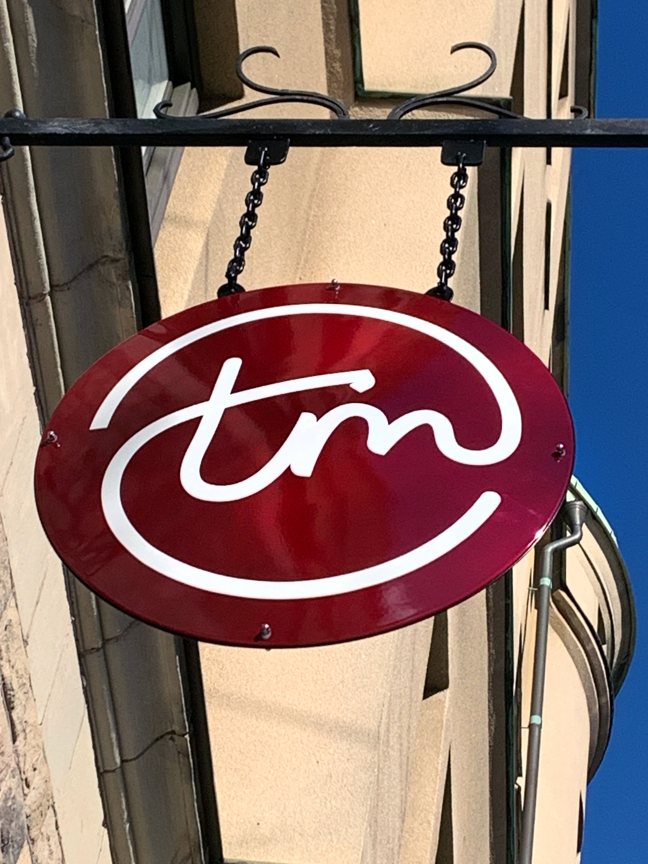 Hanging sign with a red circular background and white lowercase "tm" logo above a building entrance. TBD, To Be Designed strategic design studio in Stockholm making beautiful design for ambitious market leaders.