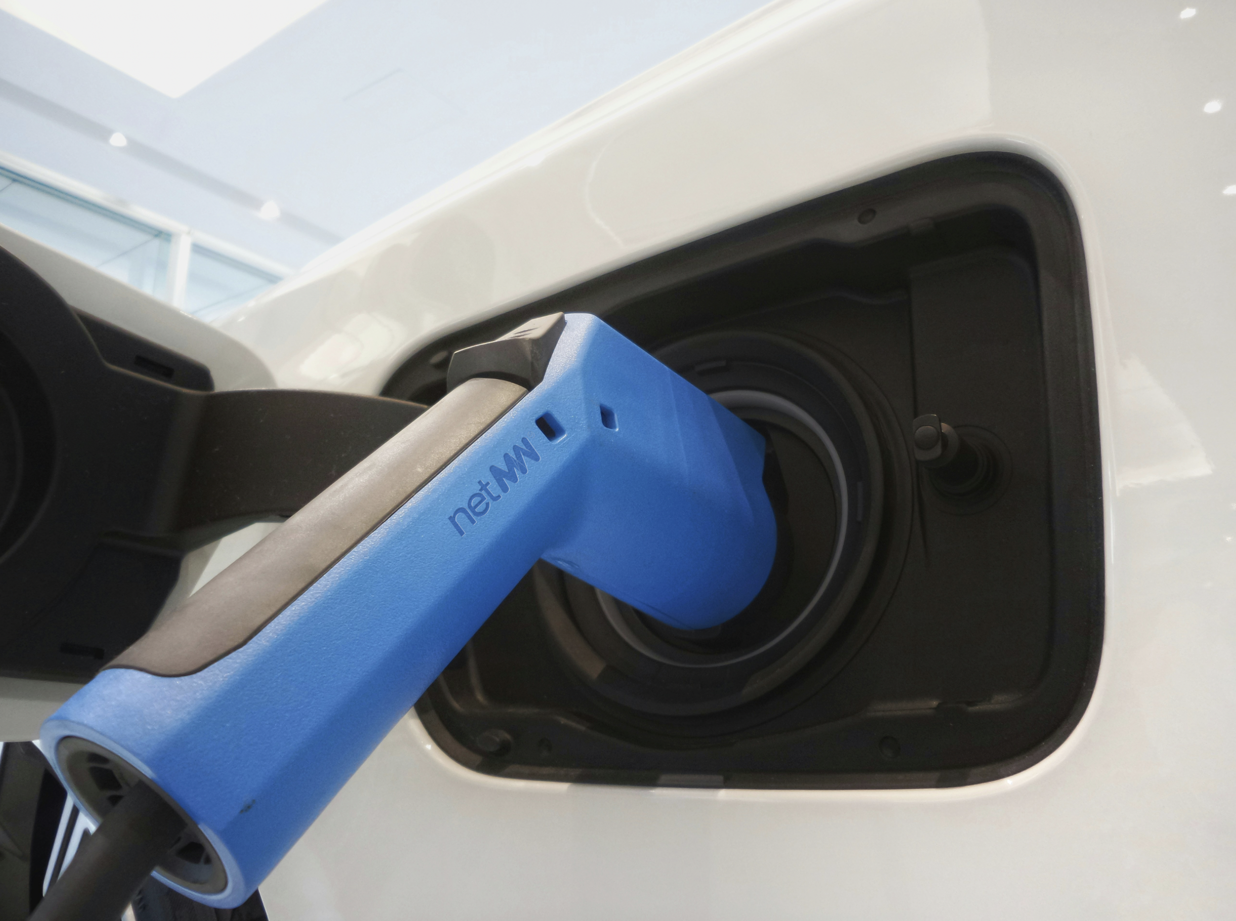 Electric vehicle charging plug inserted into a white car's charging port. Visual identity and design by TBD To Be Designed.