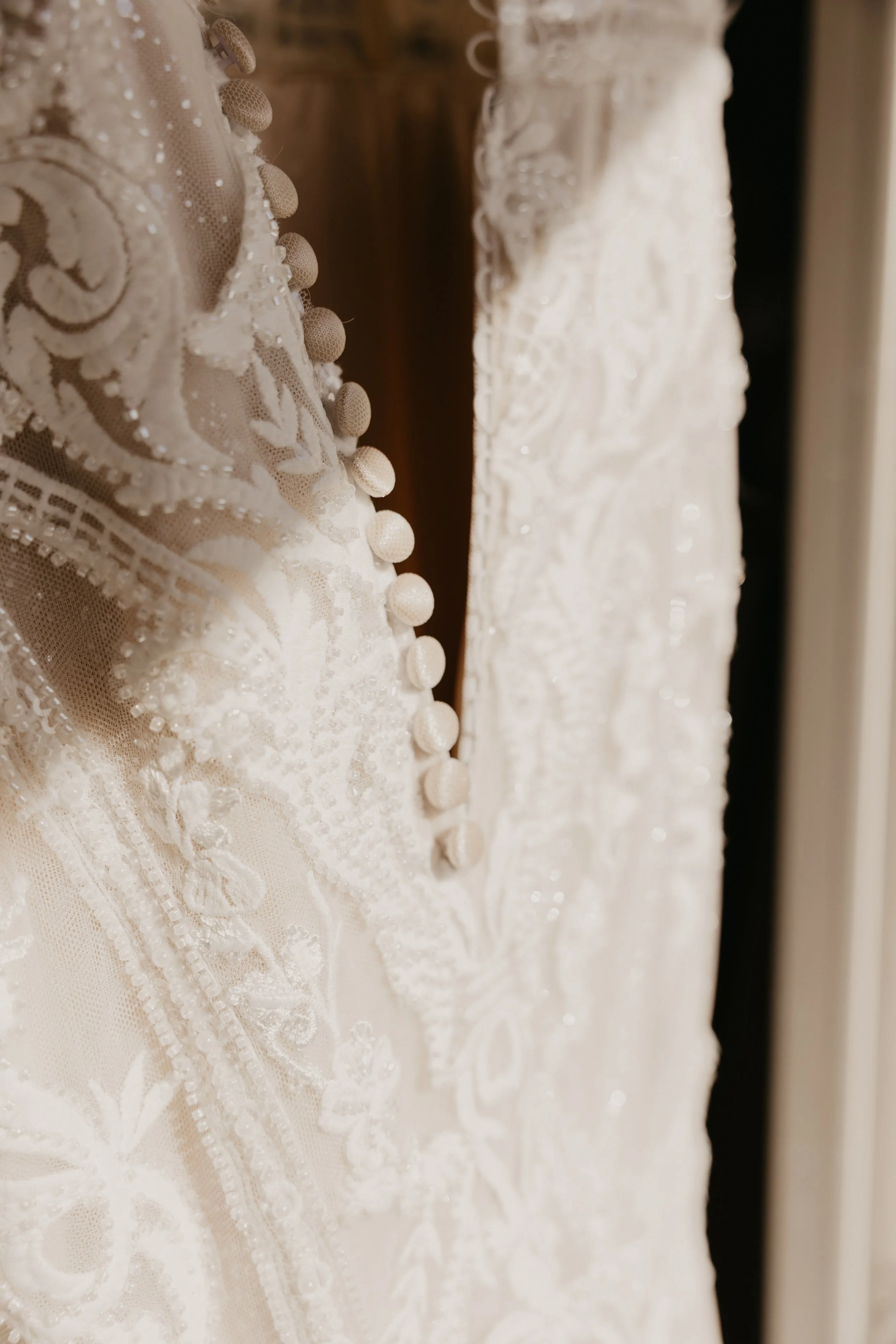 Close-up of an elegant, embroidered white wedding dress with fabric-covered buttons.