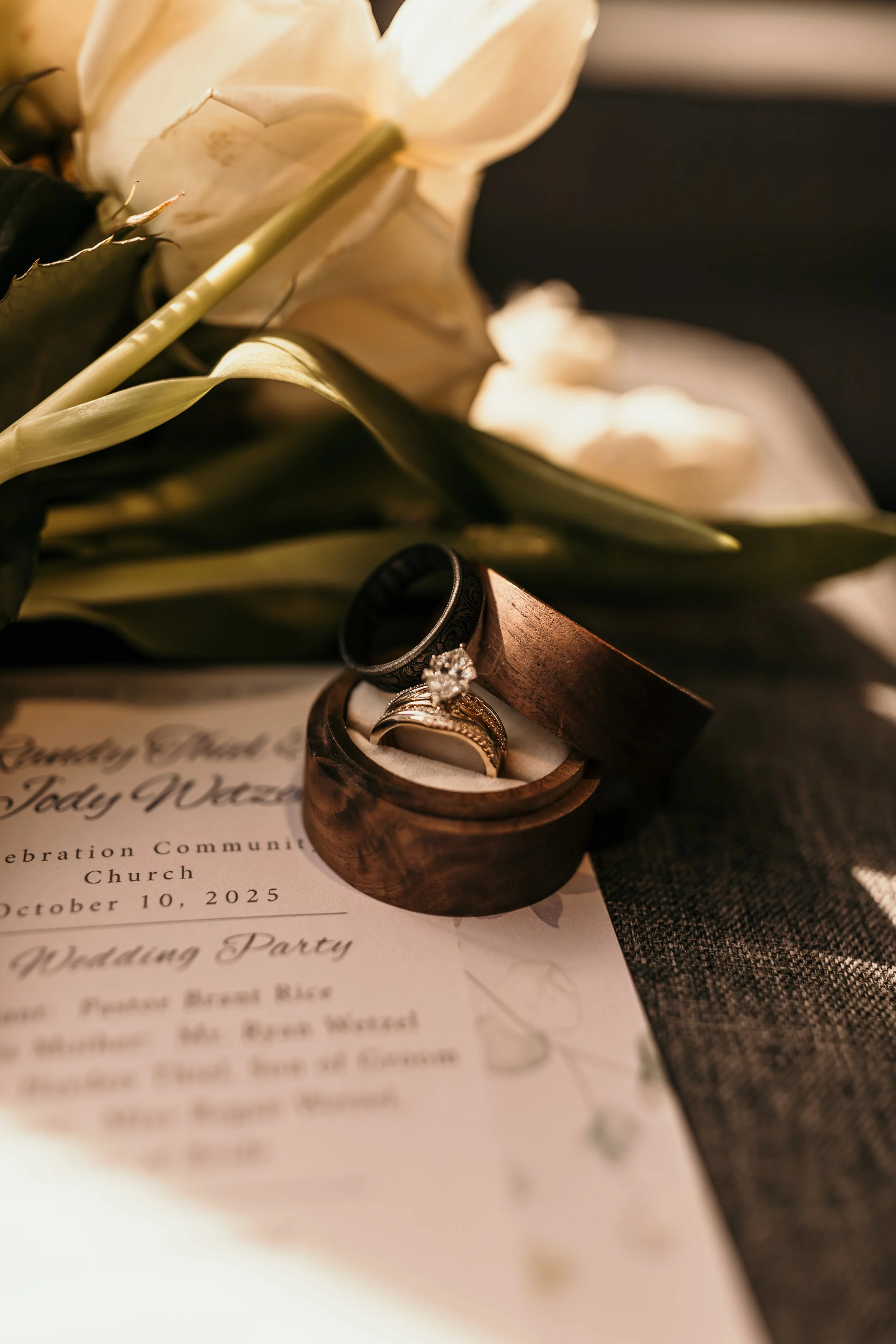 A wedding invitation card with rings and a flower on top.
