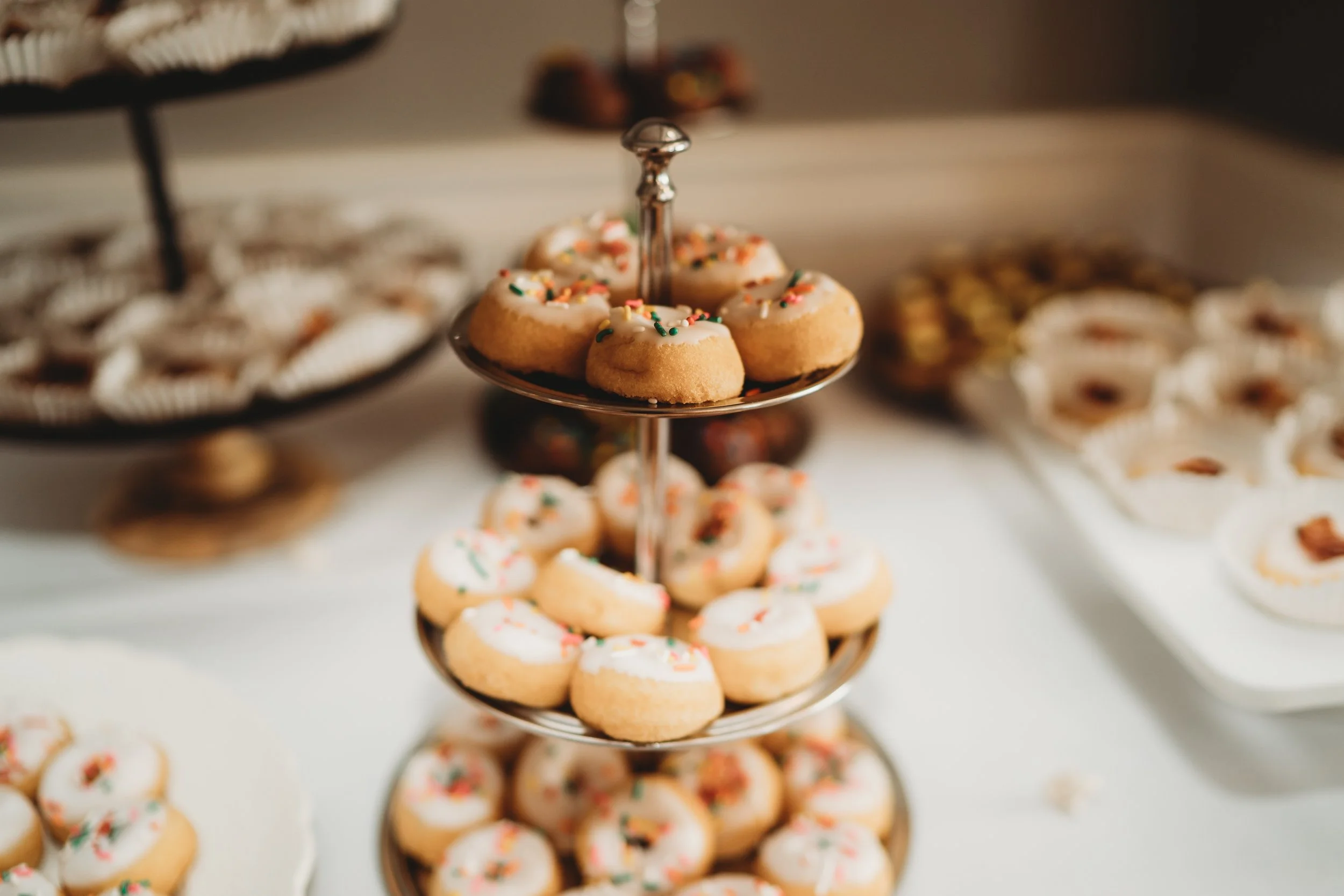 Tiered tray with decorated cookies and assorted desserts in the background.
