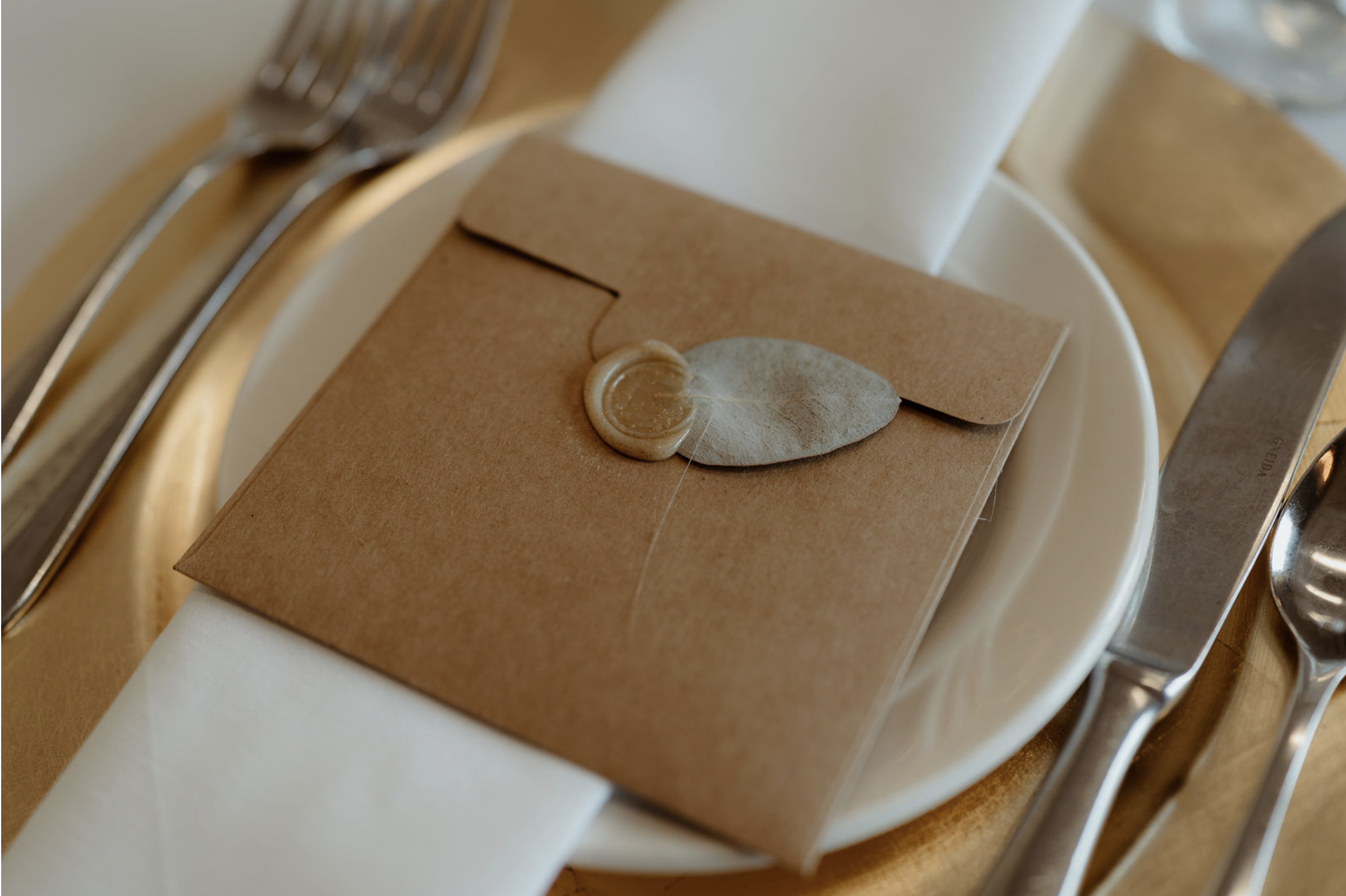 Brown envelope with wax seal on a white napkin at a place setting with silverware.