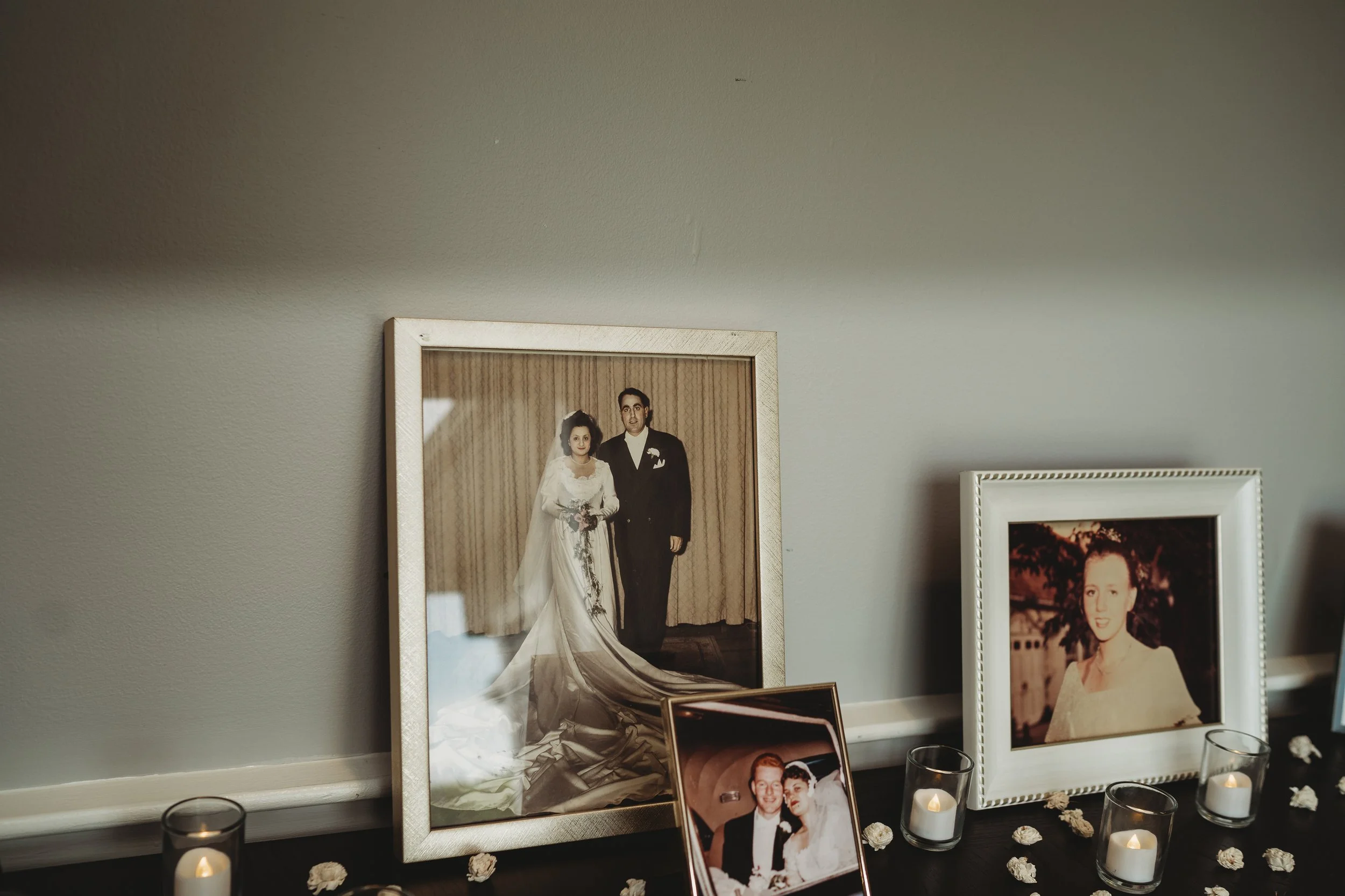 A display of framed wedding photos with candles and small flowers on a dark surface.