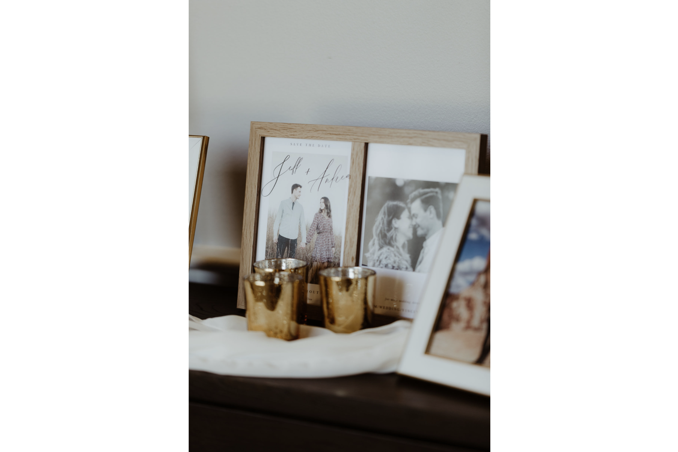 Decorative photo display with framed photos, including a save-the-date engagement photo of a couple, and gold candles on a cloth-covered surface.