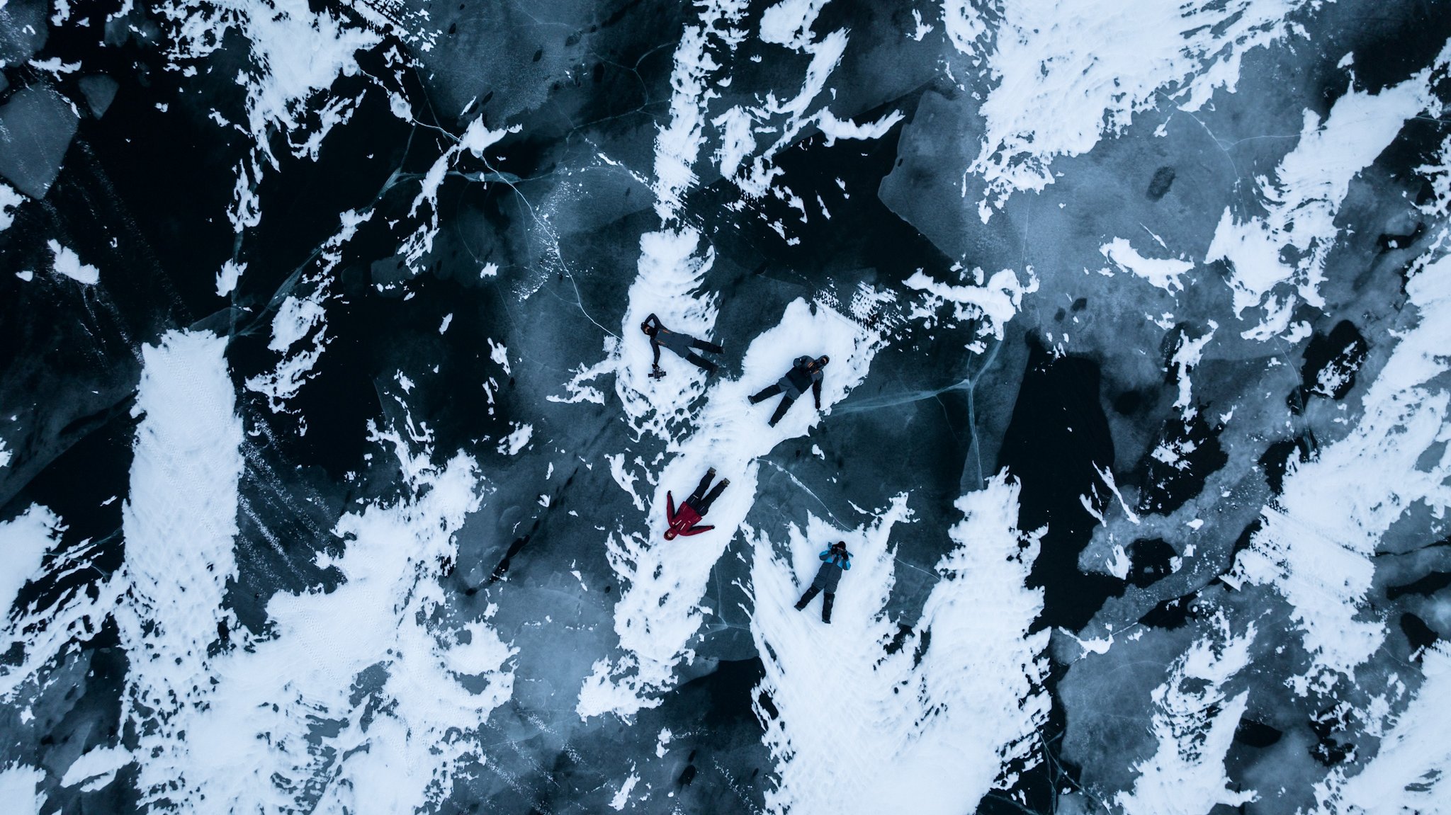 An aerial view of climbers resting on a snowy, icy mountain slope with dark rock formations.