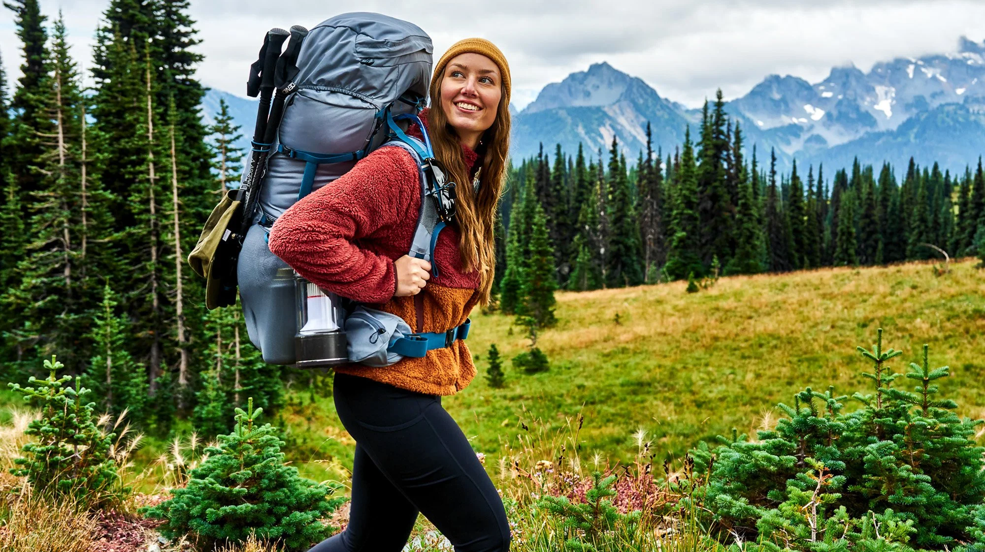 A woman hiking through a forested mountain area, carrying a large backpack.