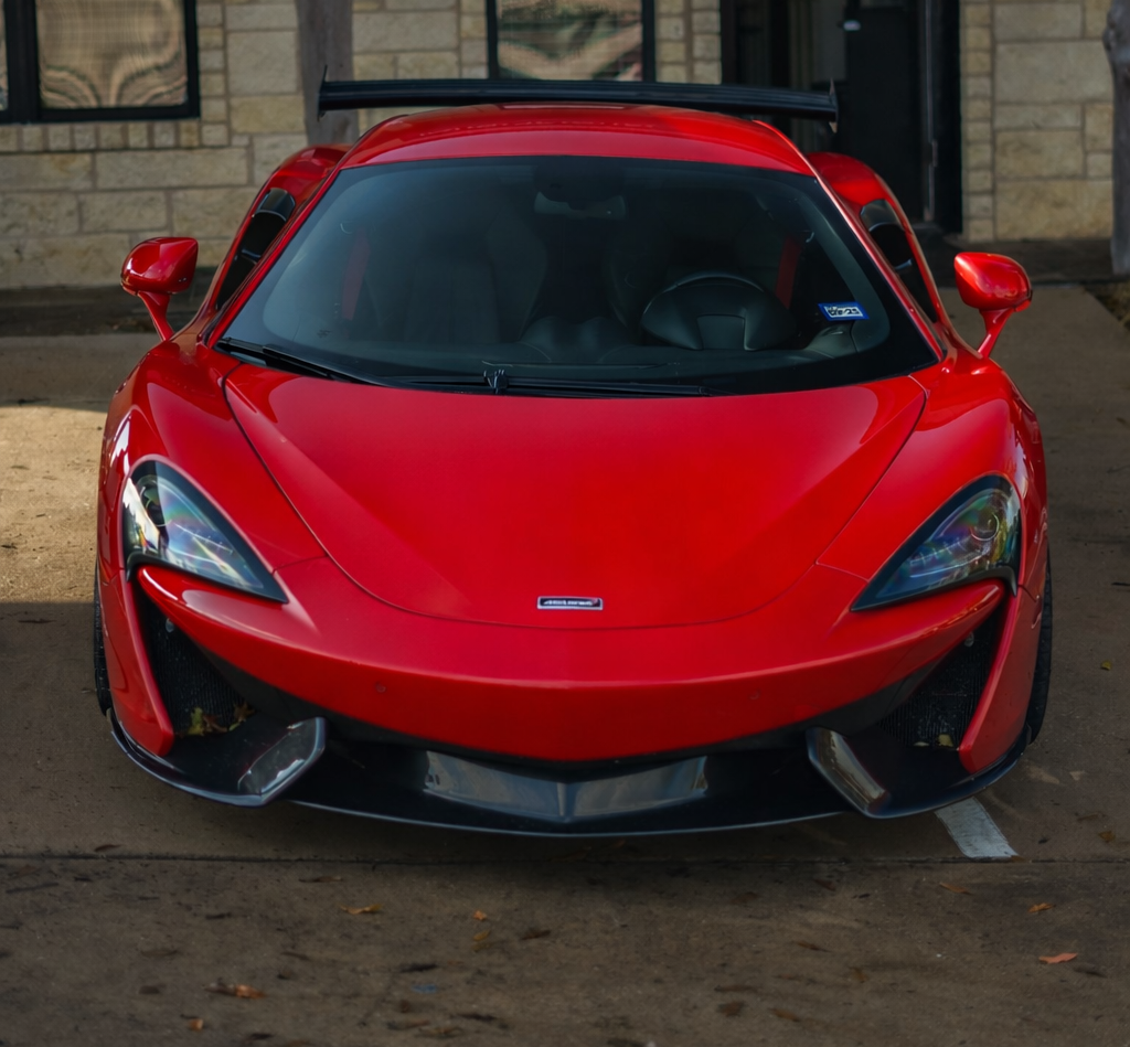 Red sports car parked on a concrete surface in front of a stone wall.