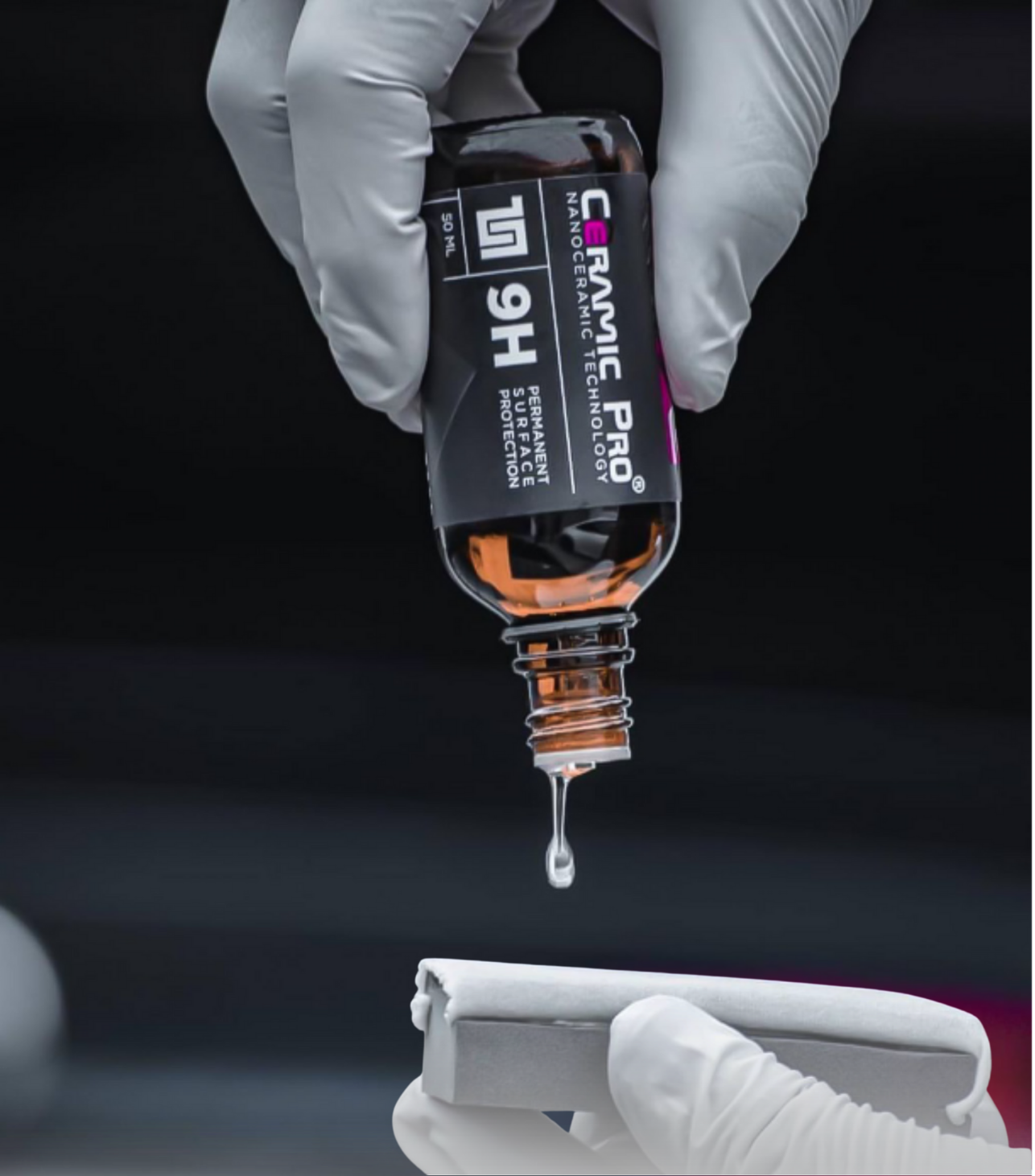 Close-up of a hand in a white glove holding a bottle of ceramic pro coating, with a droplet about to fall onto a surface.