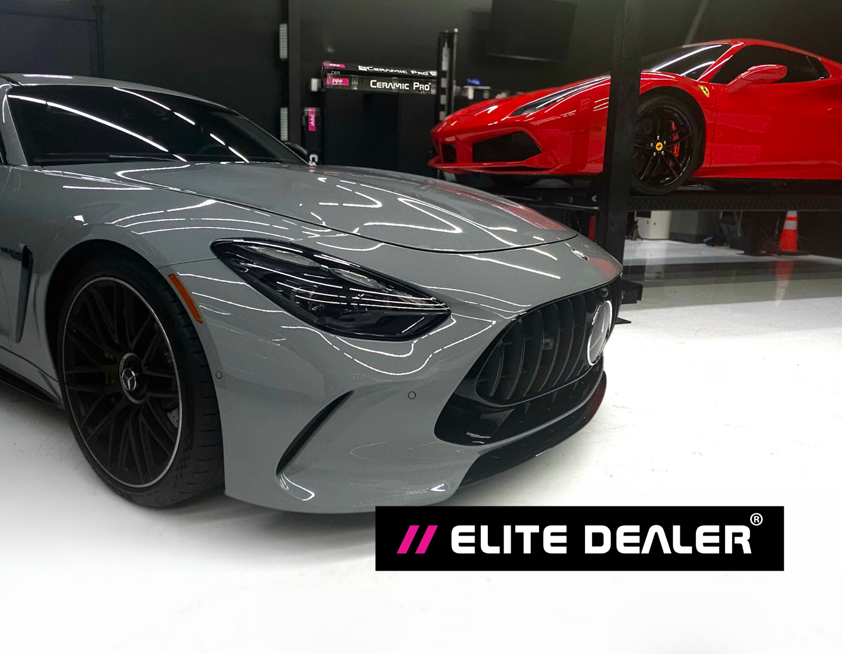 A silver luxury sports car in the foreground with a red sports car on a lift in the background at an Elite Dealer showroom.