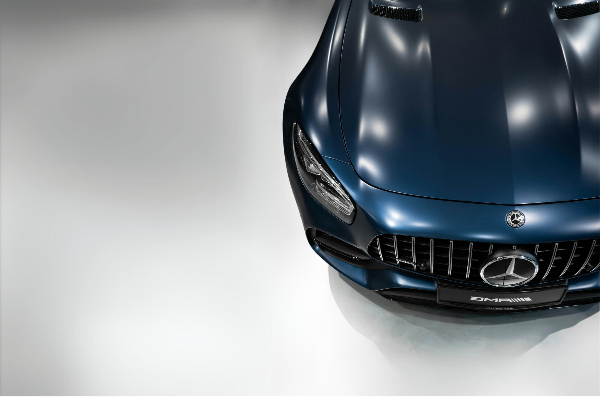 Close-up of the front of a dark blue Mercedes-AMG sports car, showing the headlight, grille, and Mercedes emblem.