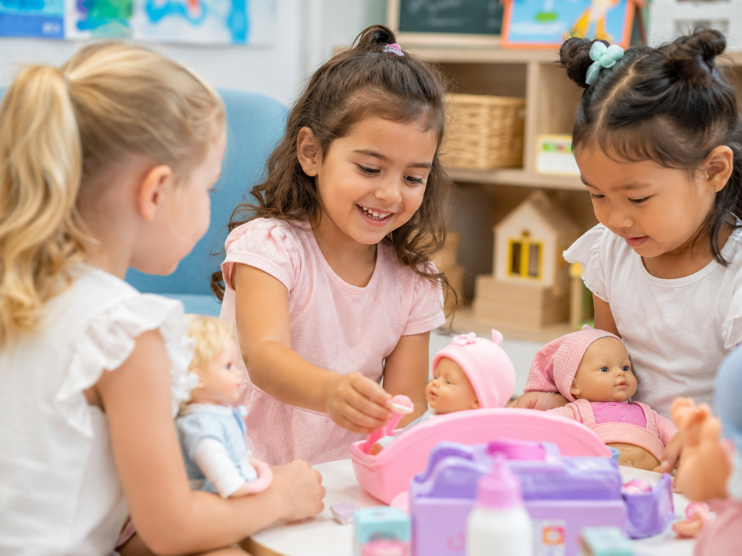 Four young children sitting on a wooden floor, playing with colorful building blocks in a well-lit room with shelves and a plant in the background.