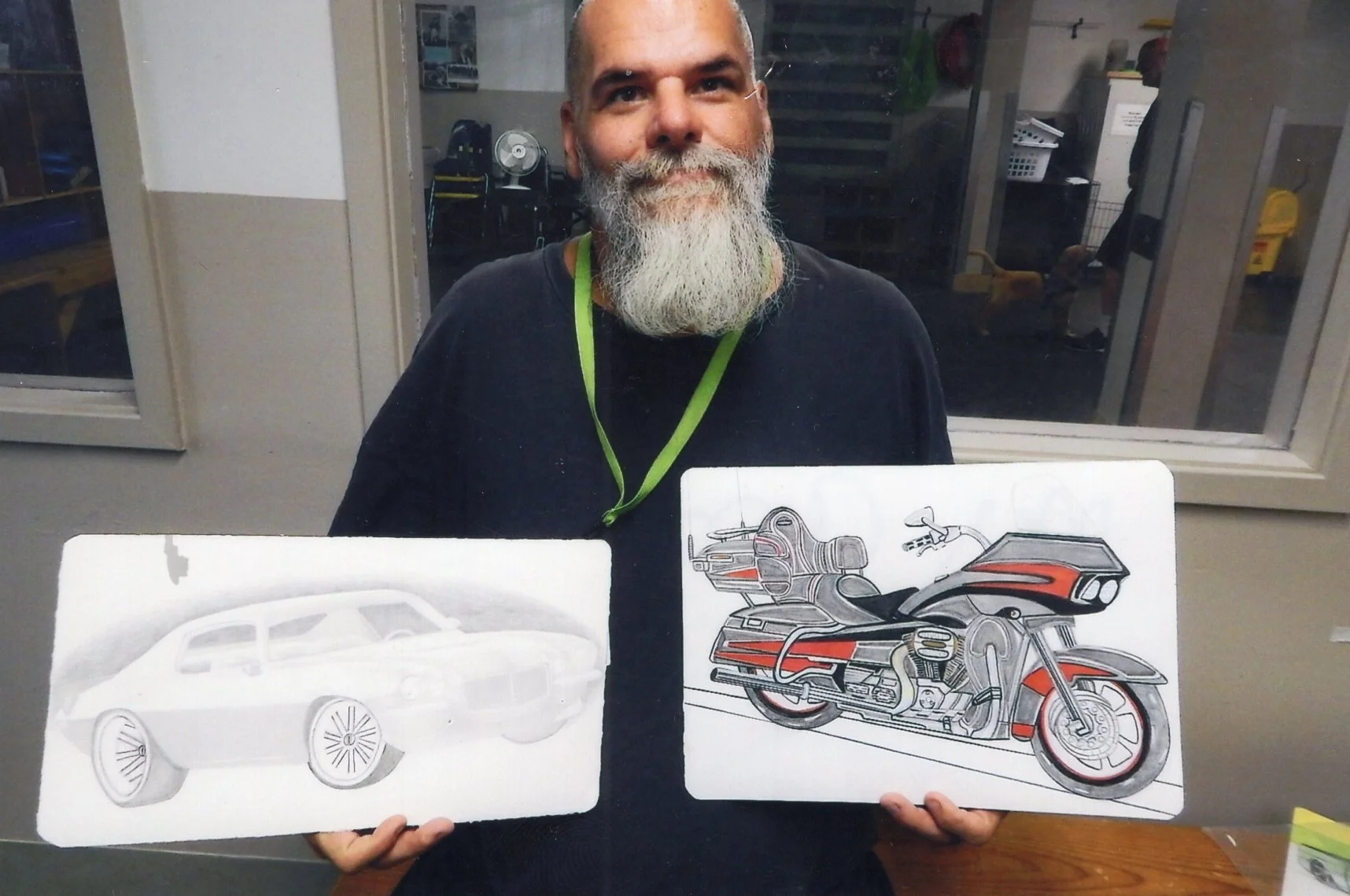 The artist is holding up two drawings -- one is of a svintage sports car. The other is a highly detailed drawing of a motorcycle.