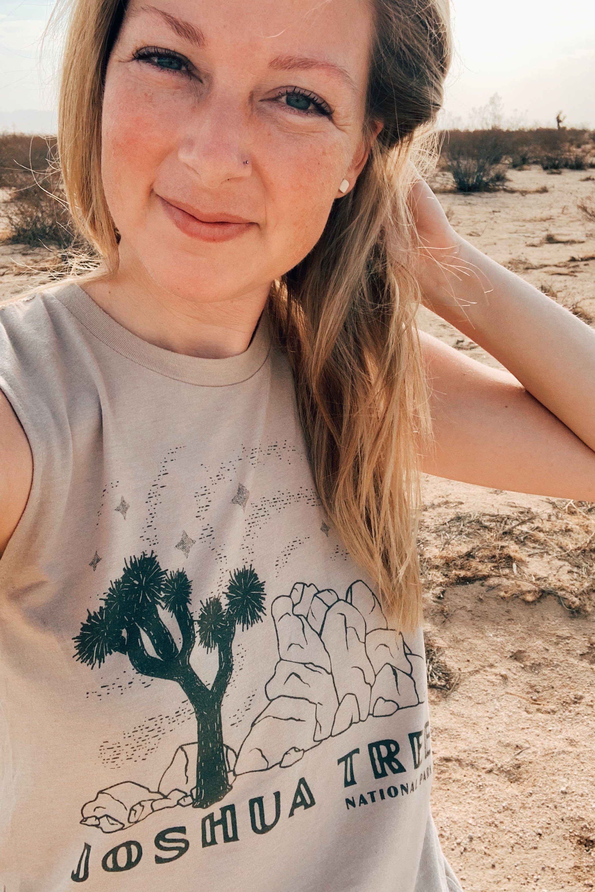 A blonde woman modeling the Joshua Tree shirt. Behind her is Joshua Tree National Park