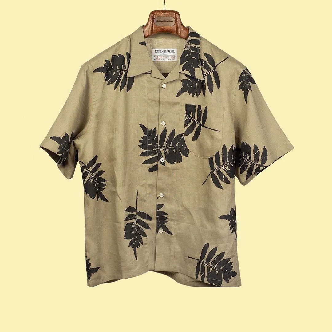 A short sleeve camp collar shirt in a tan color, with black screen printed ferns