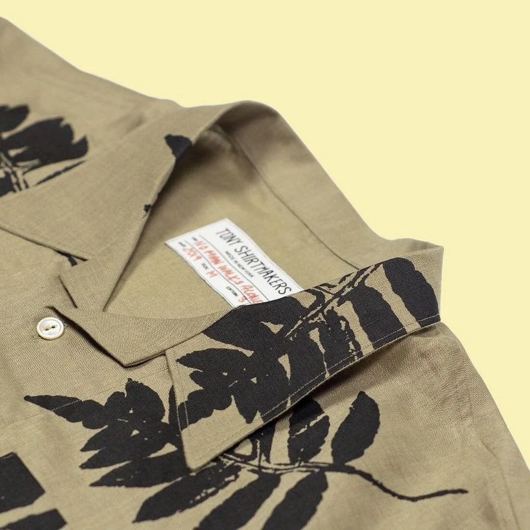 A close up of a tan shirt with black ferns printed on it, designed by Bang