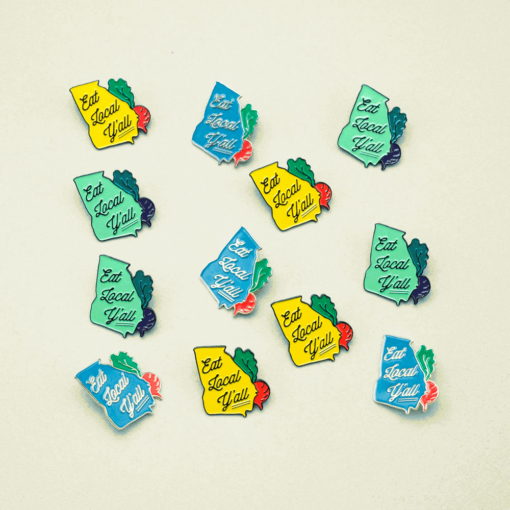 Enamel pins dance around in an animation. The pins are shaped like the state of Georgia and say Eat Local Y'all with a radish on the side of the pin.