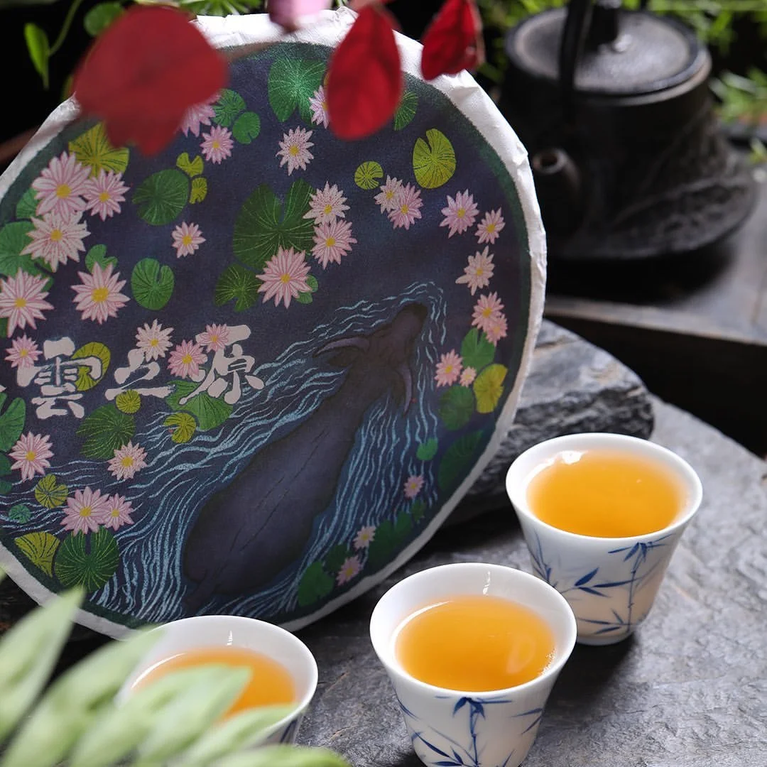 Three tea cups with golden liquid sit in front a tea cake with the Ox swimming through a river illustration