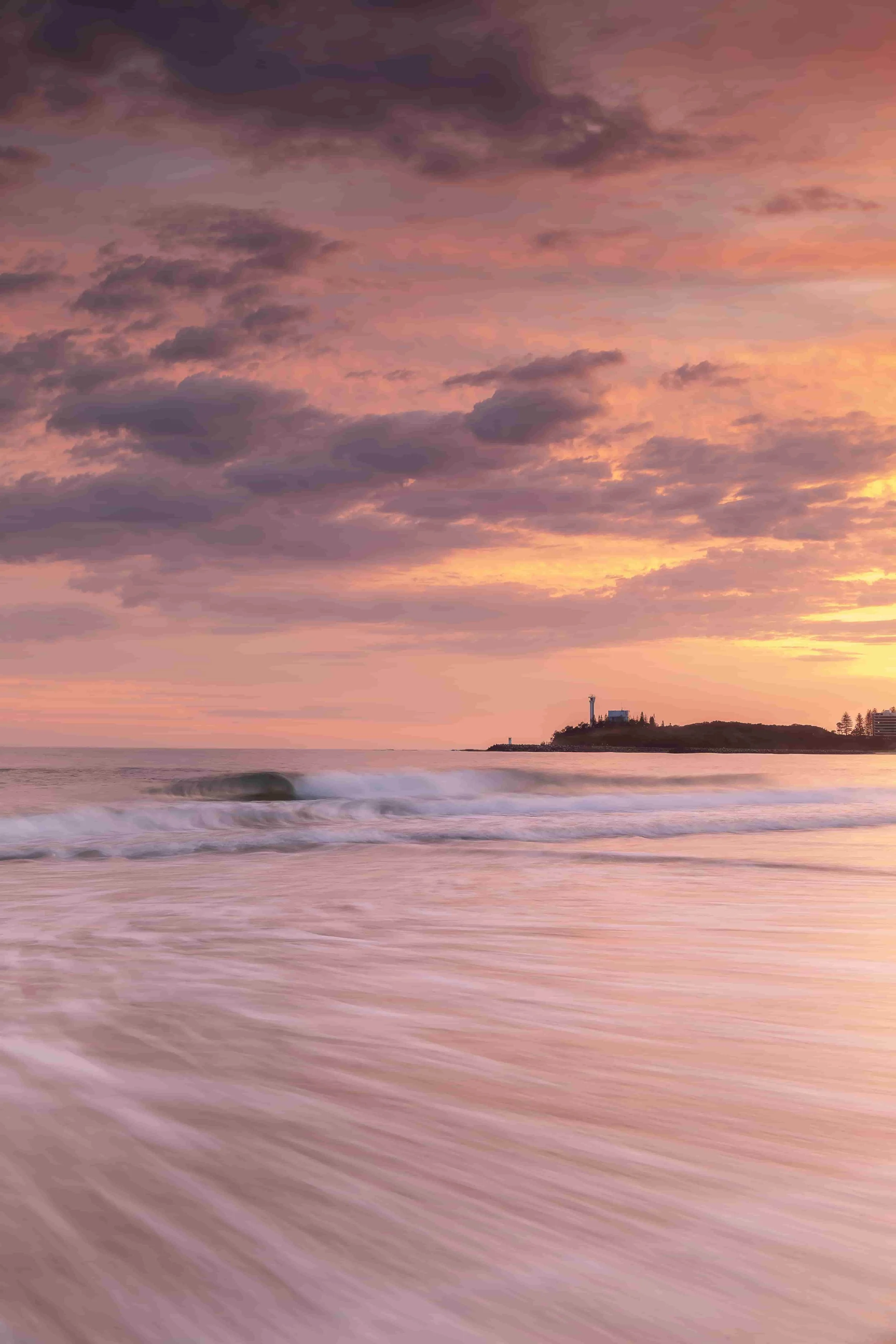 Pink sunrise over Mooloolaba Main Beach on the Sunshine Coast, with waves and soft pink light reflected across the wet sand.