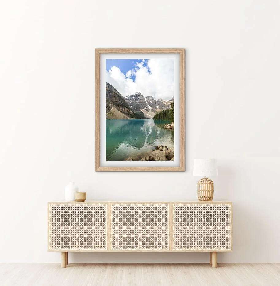 Framed Moraine Lake Canadian Rockies landscape photography print displayed above a rattan sideboard in a modern interior