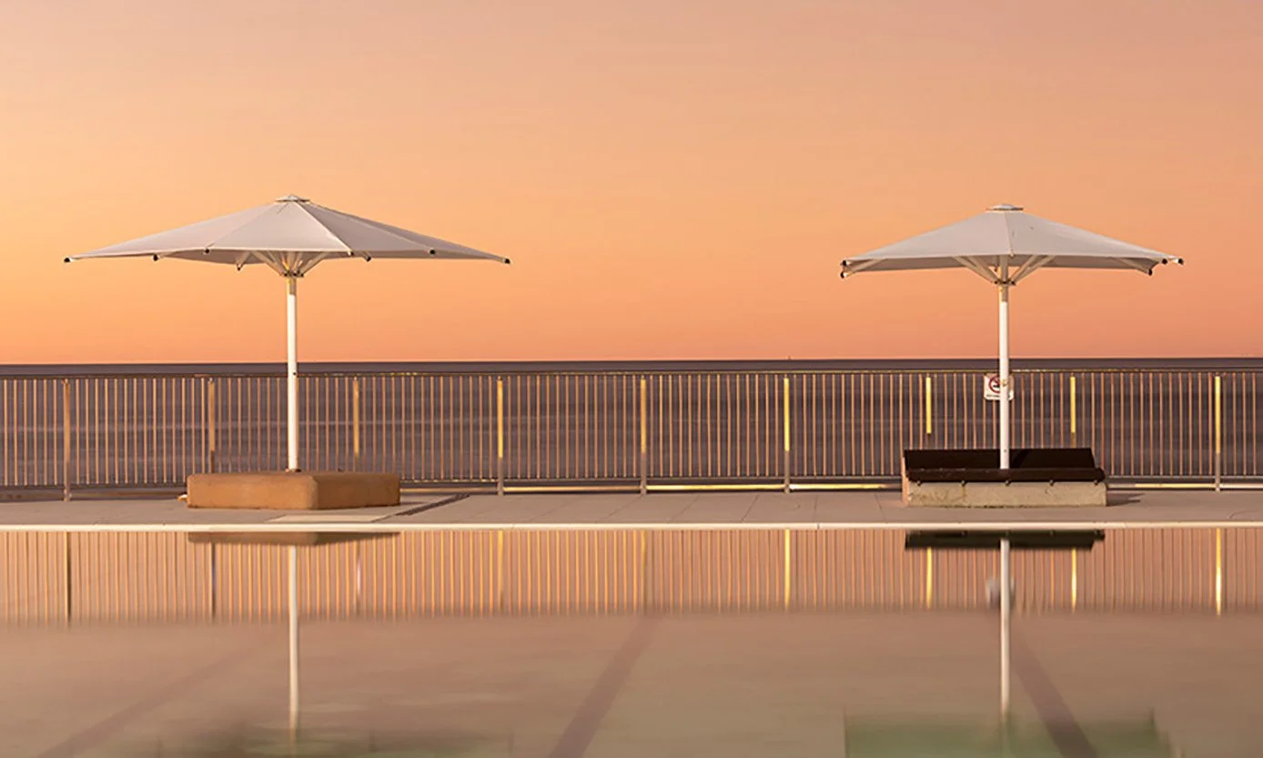 White umbrellas reflected in the calm water of the Cotton Tree Ocean Pool at sunrise on the Sunshine Coast, Queensland.