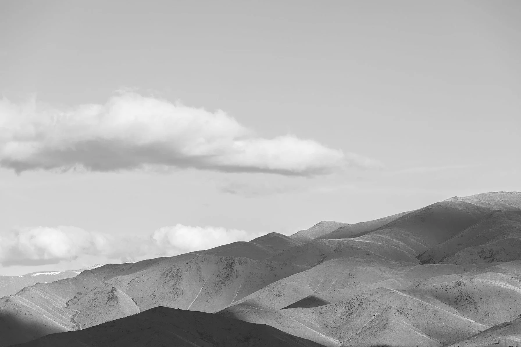 Black-and-white landscape of rolling hills and mountains under a cloudy sky.