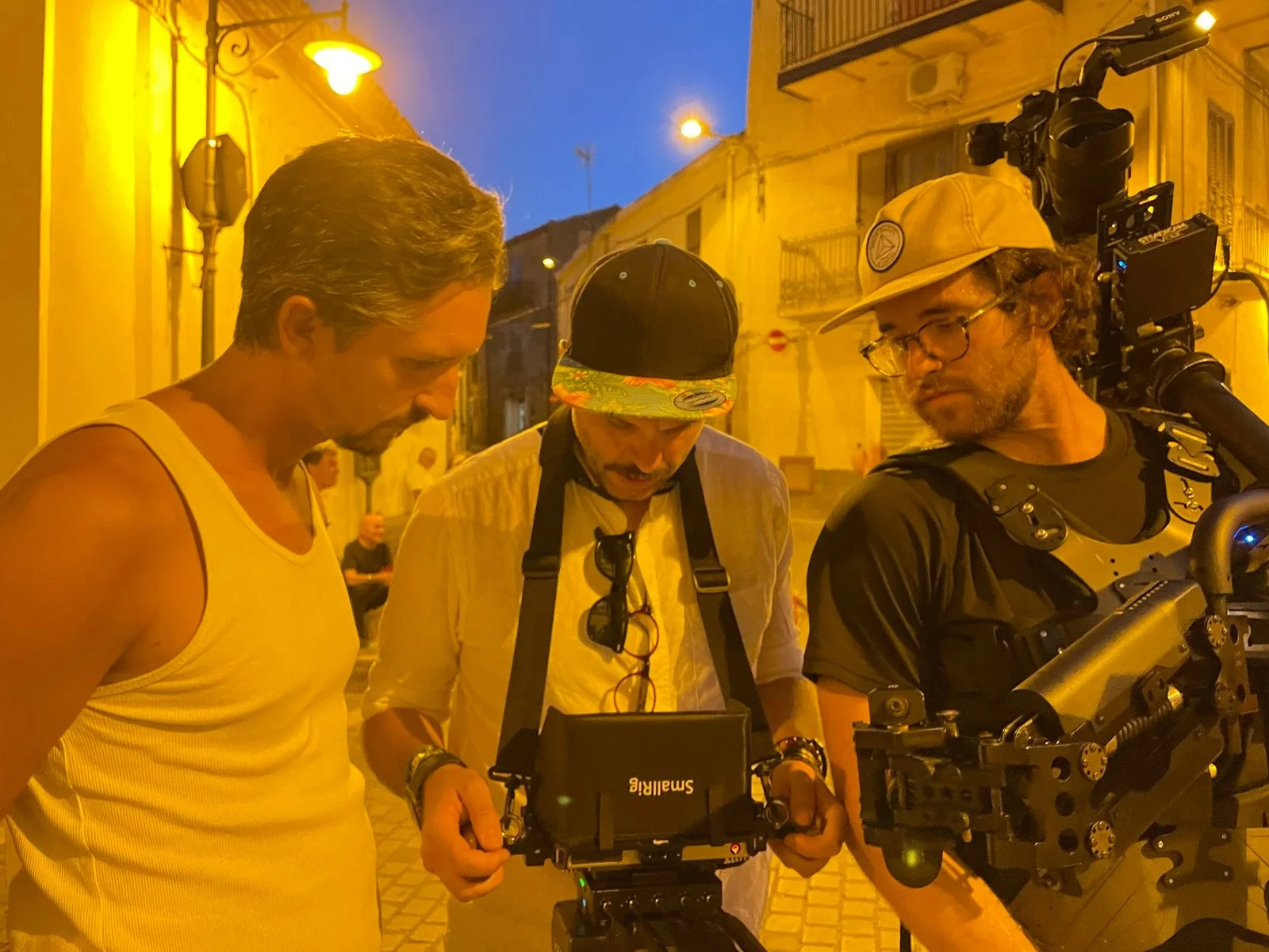 Three men on a city street during the evening, engaging with filming equipment including a camera and monitor.