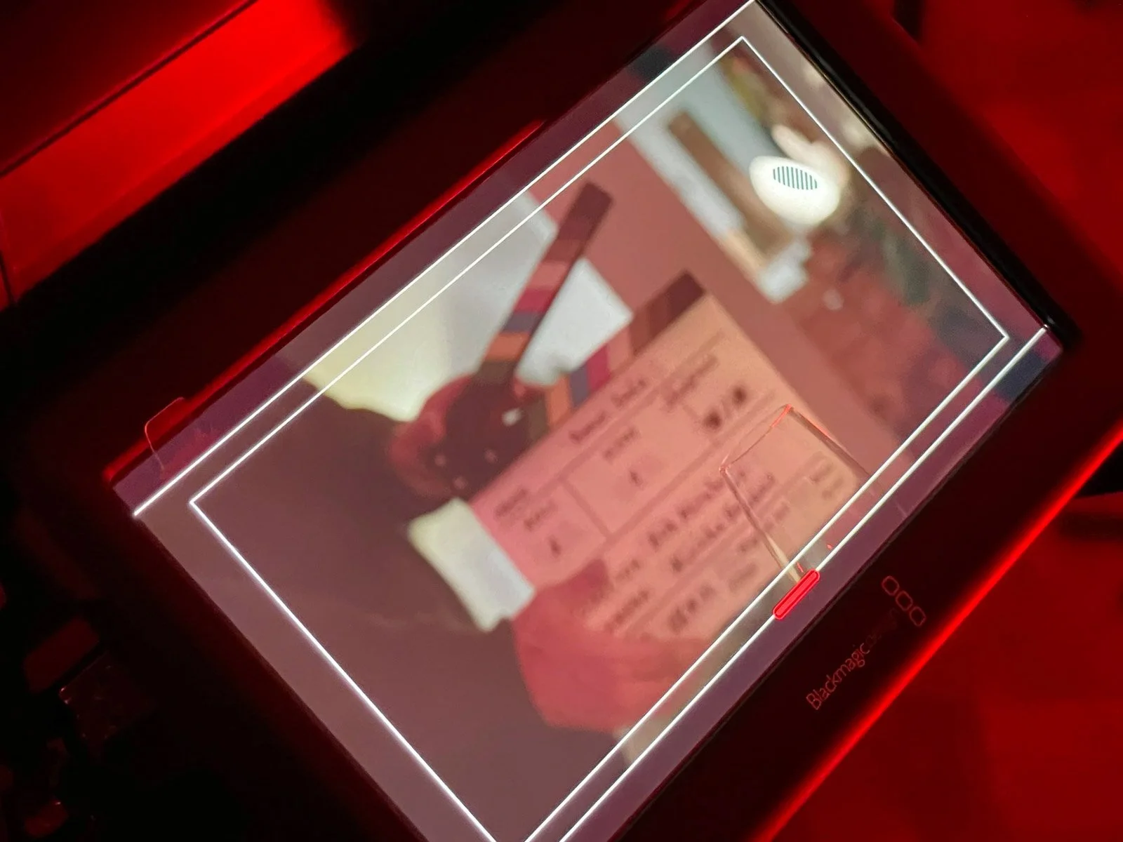 A close-up of a device screen with a blurred image of a robotic arm or mechanical device and some text or UI elements on a pinkish background, surrounded by a glowing red light.