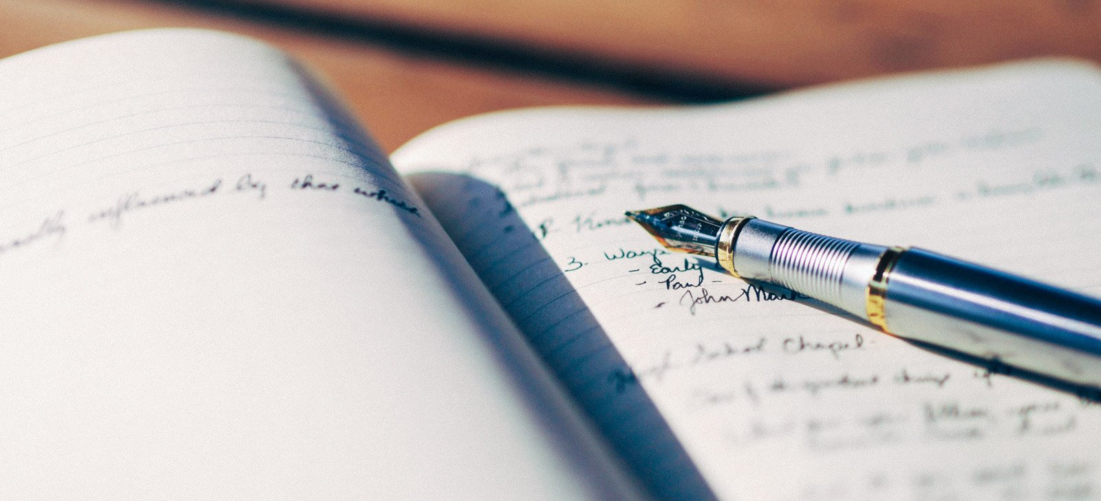 An open notebook with handwritten notes and a silver fountain pen resting on the pages.