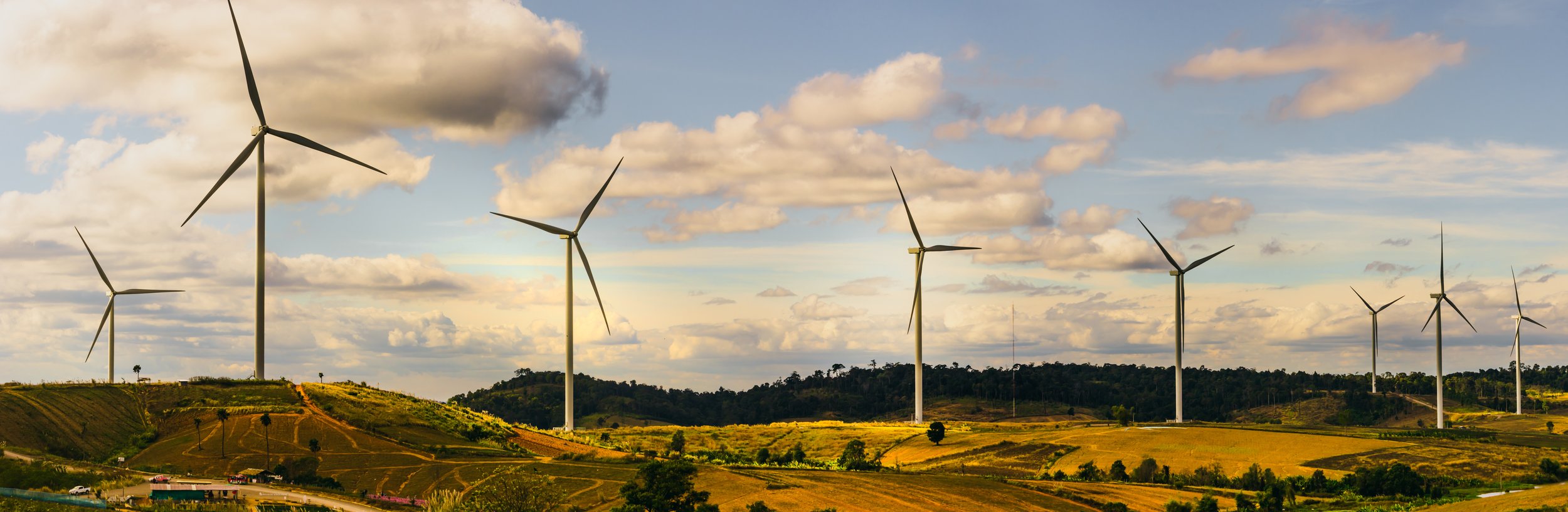 A landscape featuring multiple wind turbines on rolling hills with a partly cloudy sky.