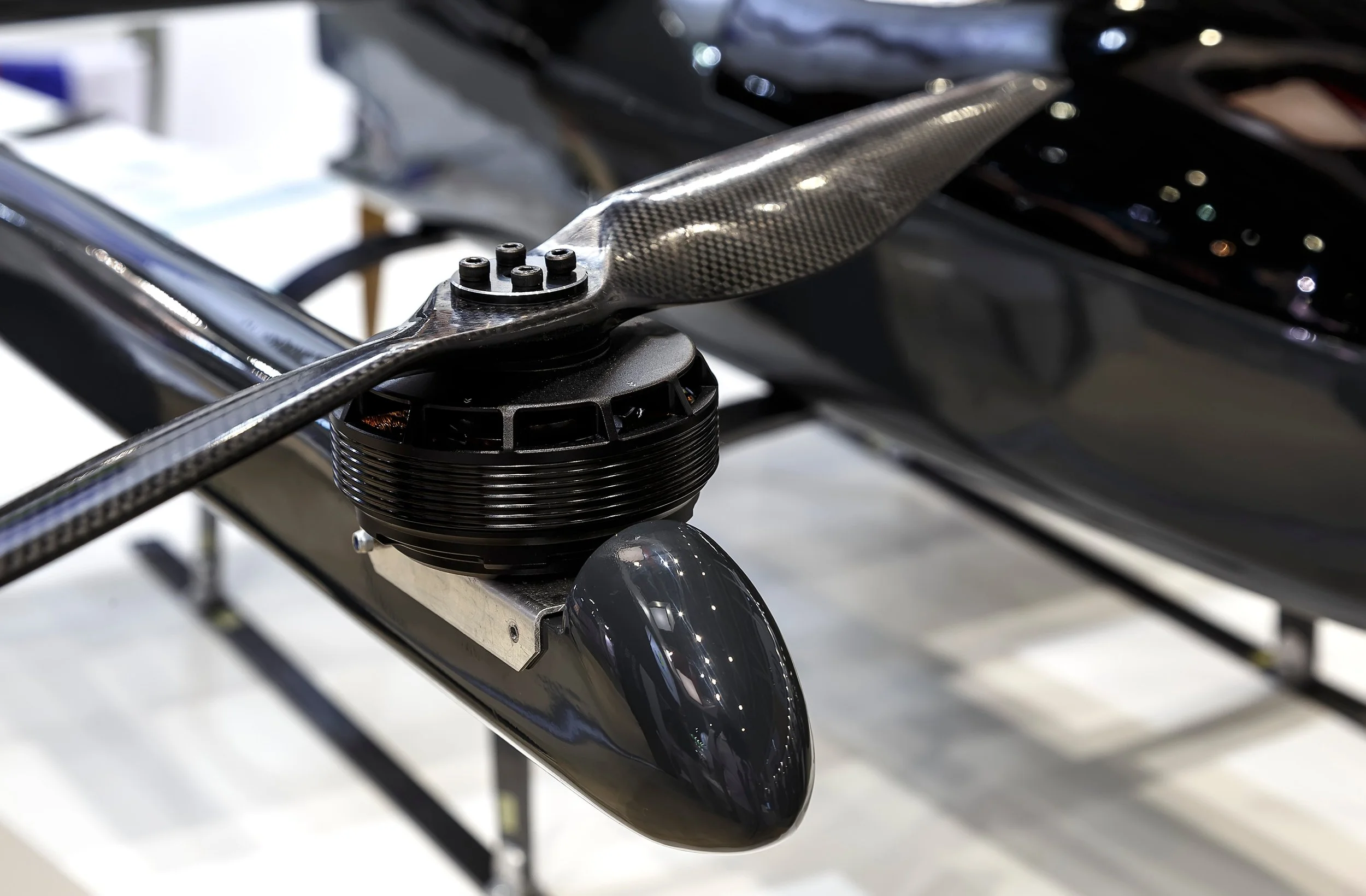 Close-up of a helicopter rotor blade with carbon fiber details and a black, circular rotor hub.