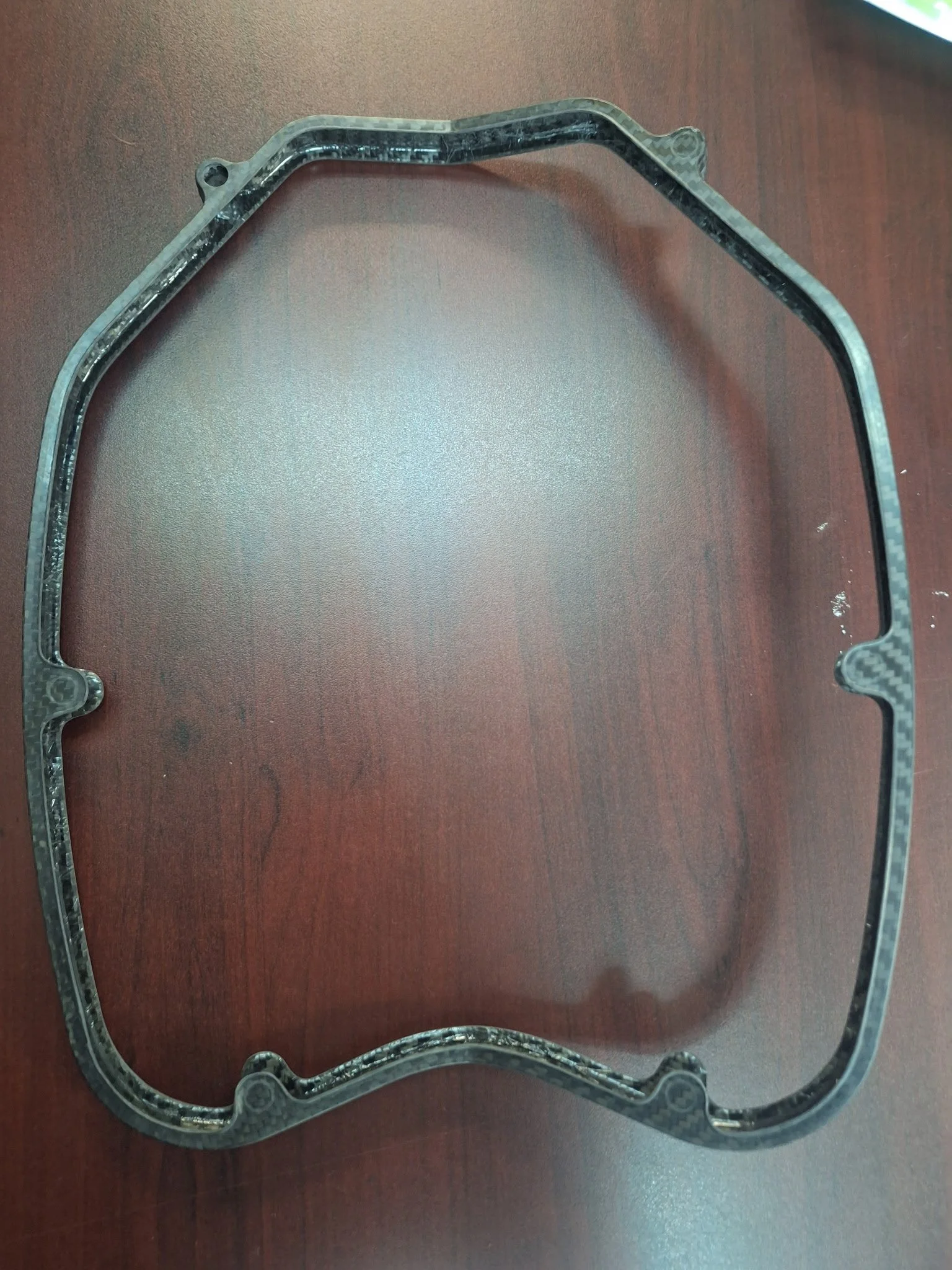 A rectangular engine gasket made of composite material laying flat on a wooden surface.