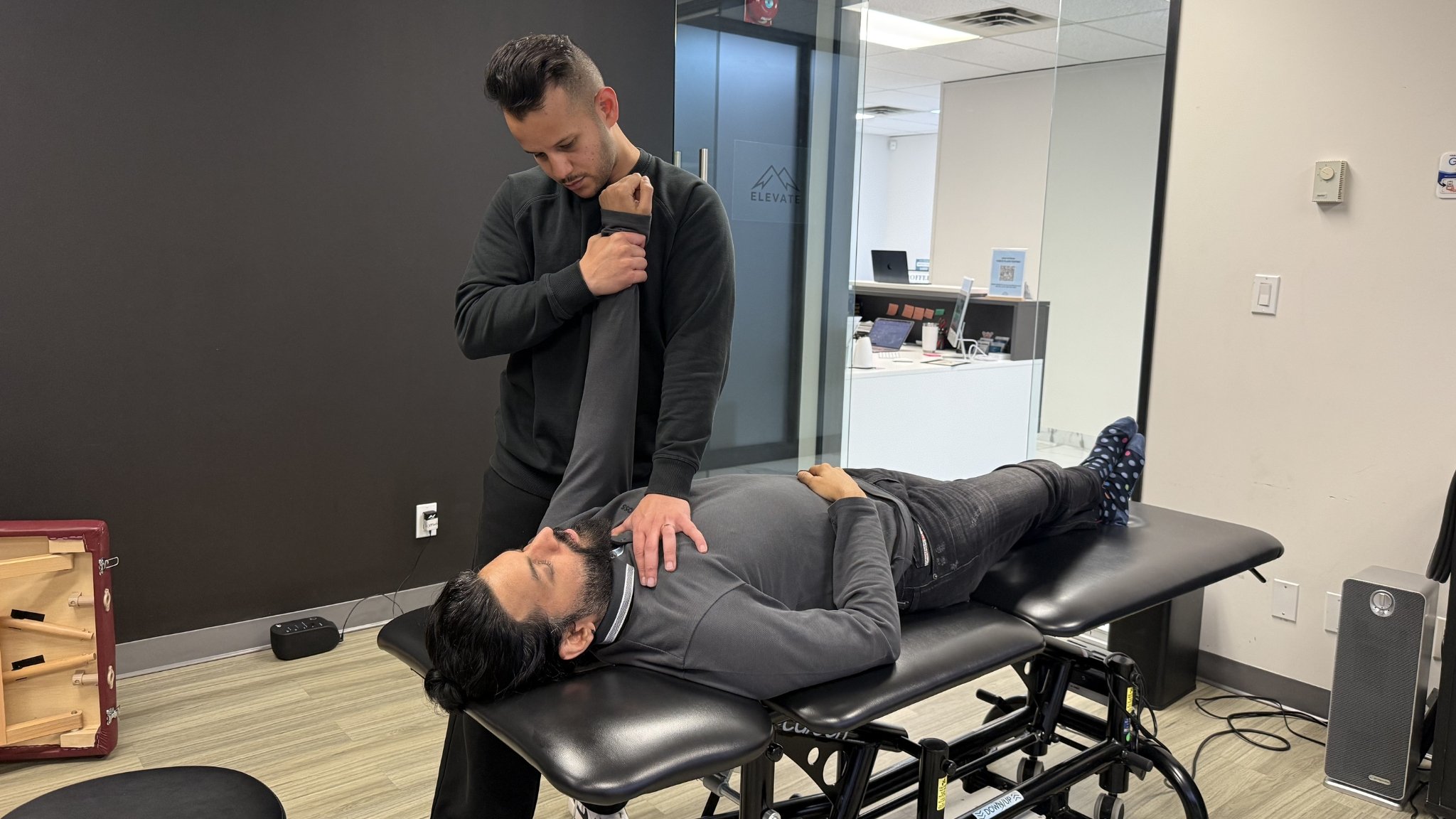 A man lying face-up on a chiropractic adjustment table receiving treatment from a chiropractic professional in an office setting.