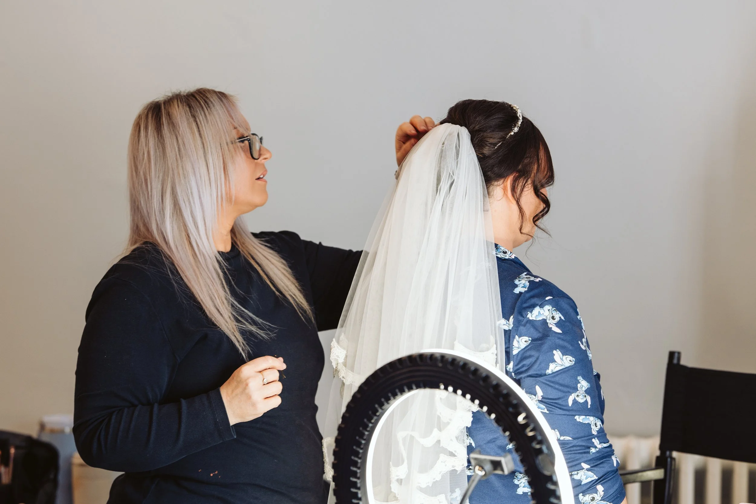 A woman in black helping a bride with her hair and veil before her wedding.