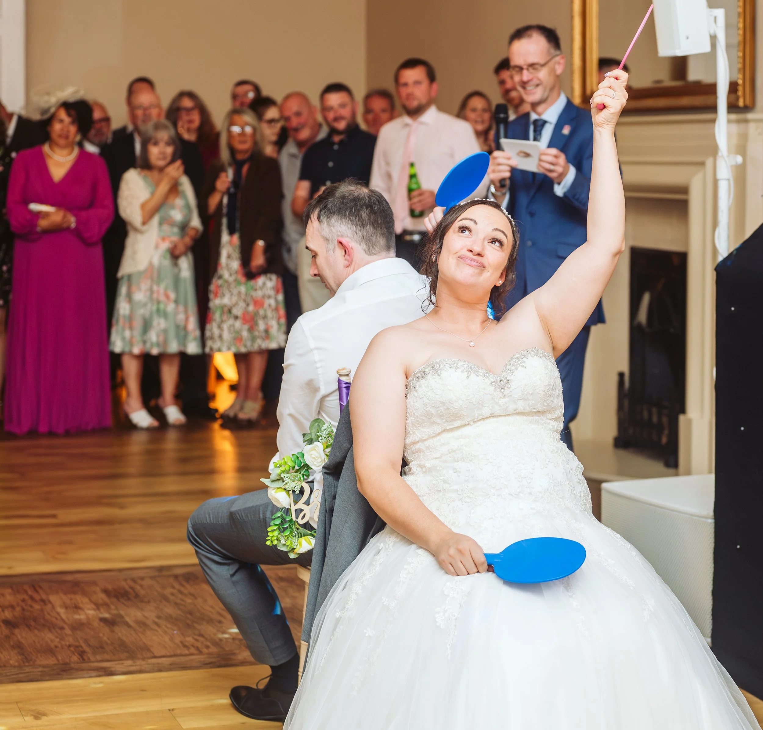 Bride and groom playing spin the bottle at wedding reception with guests watching.