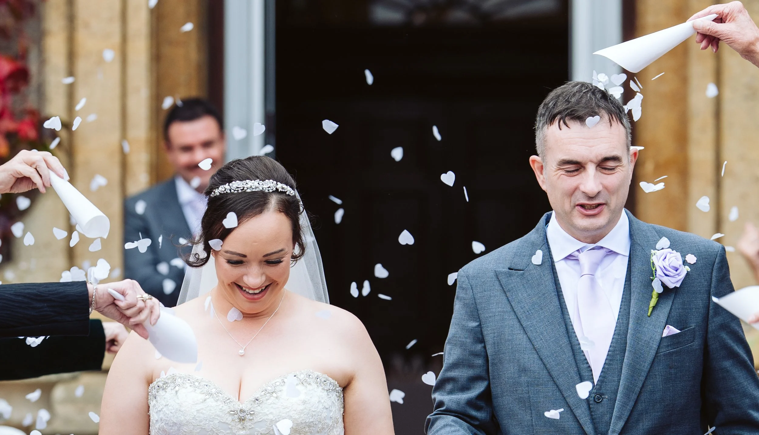 Bride and groom exiting a venue while being showered with white heart-shaped confetti.