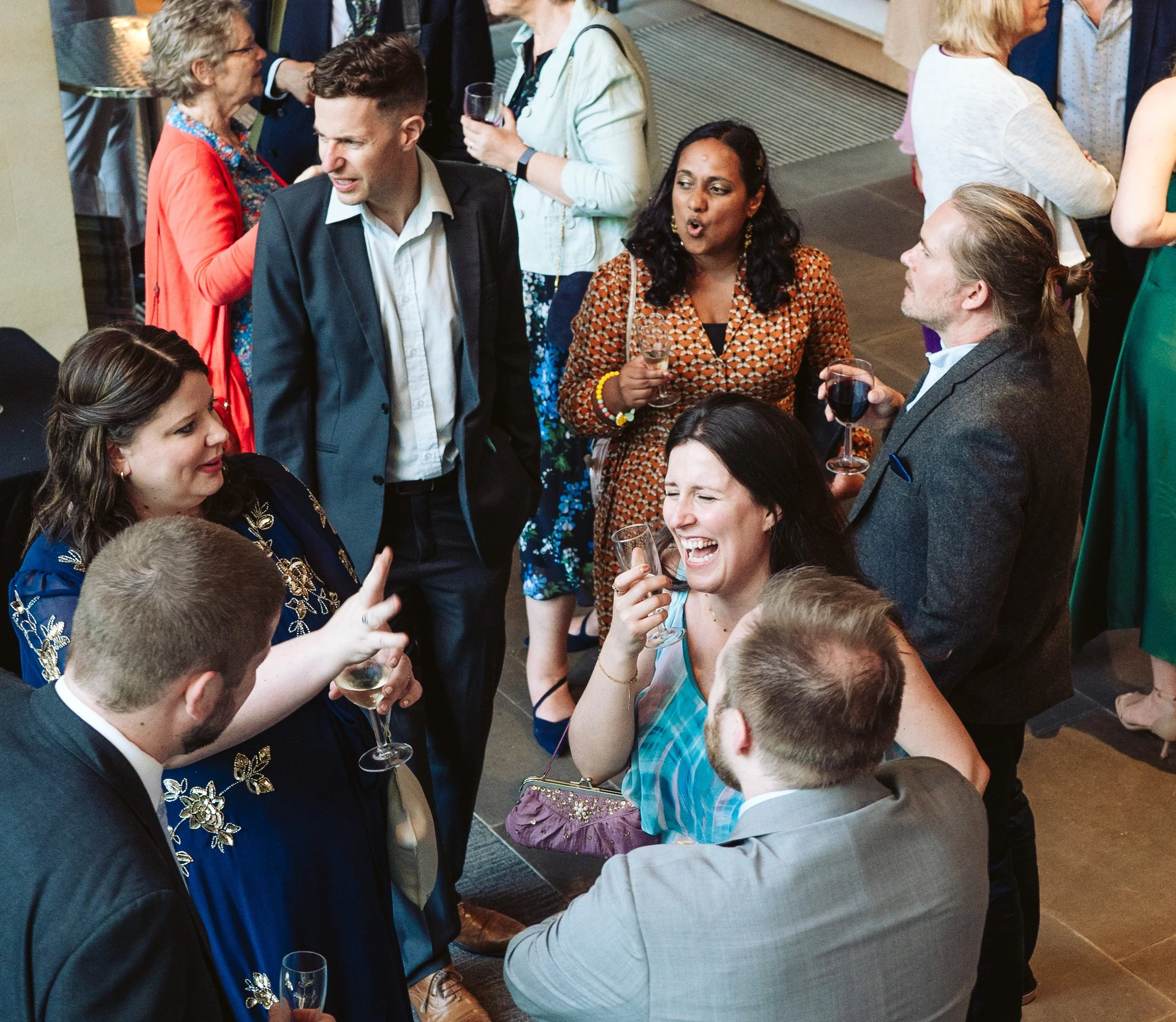 Group of people at a social gathering, talking, smiling, and holding drinks, in an indoor setting.