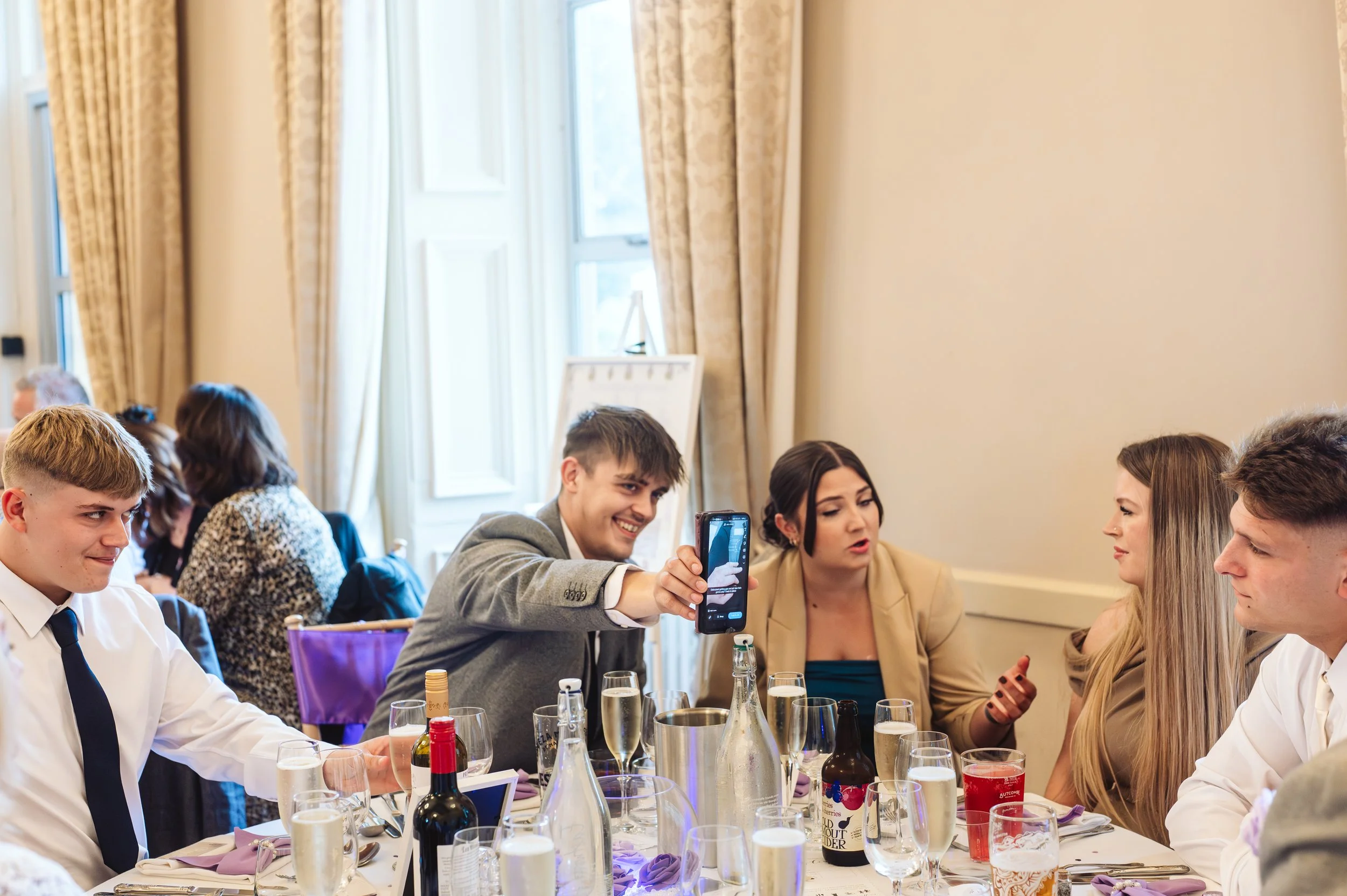 People sitting at a formal dining table, taking a selfie during a celebration or event.