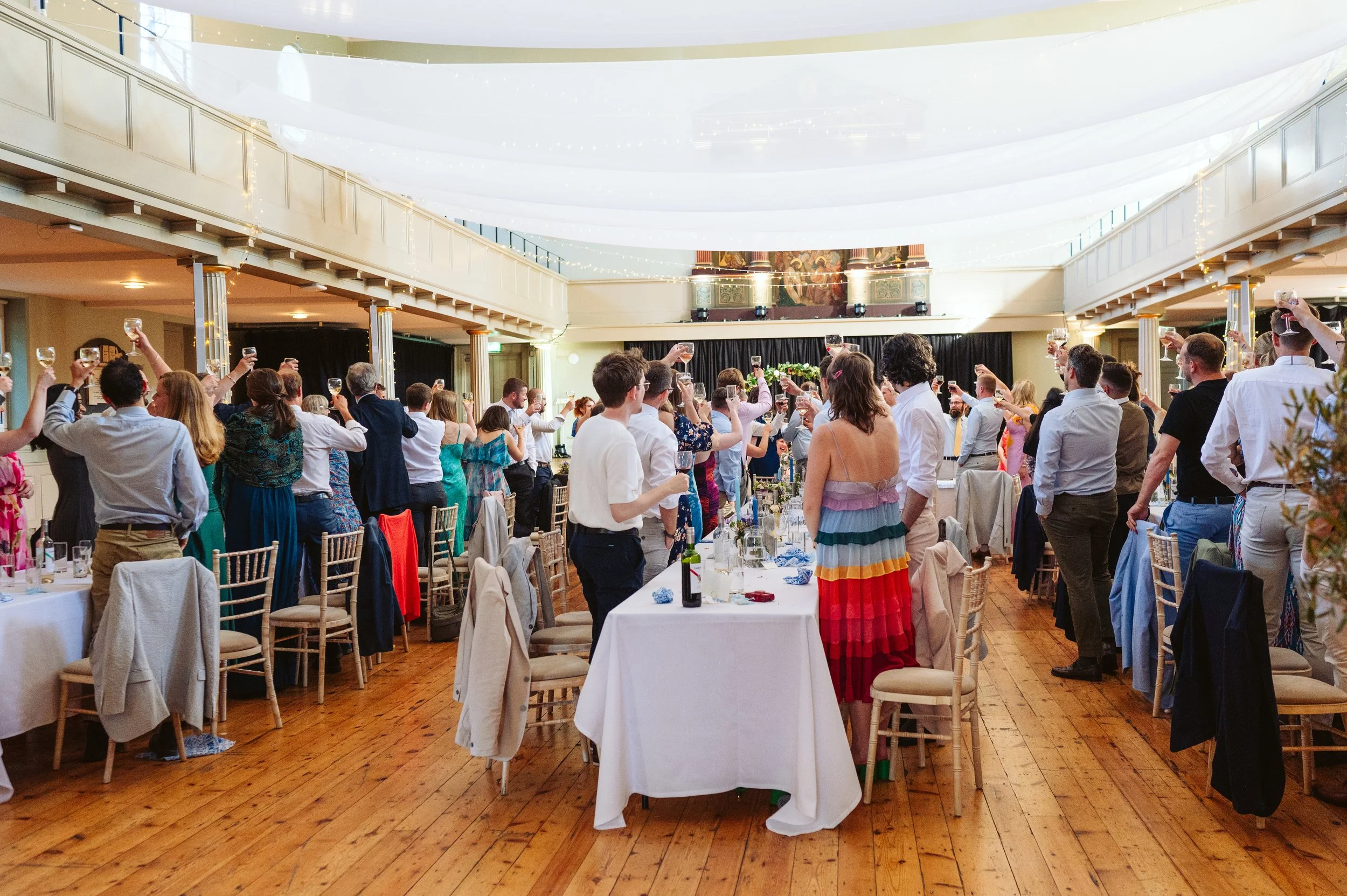 Guests at a wedding reception raising glasses in a toast in a decorated indoor venue.